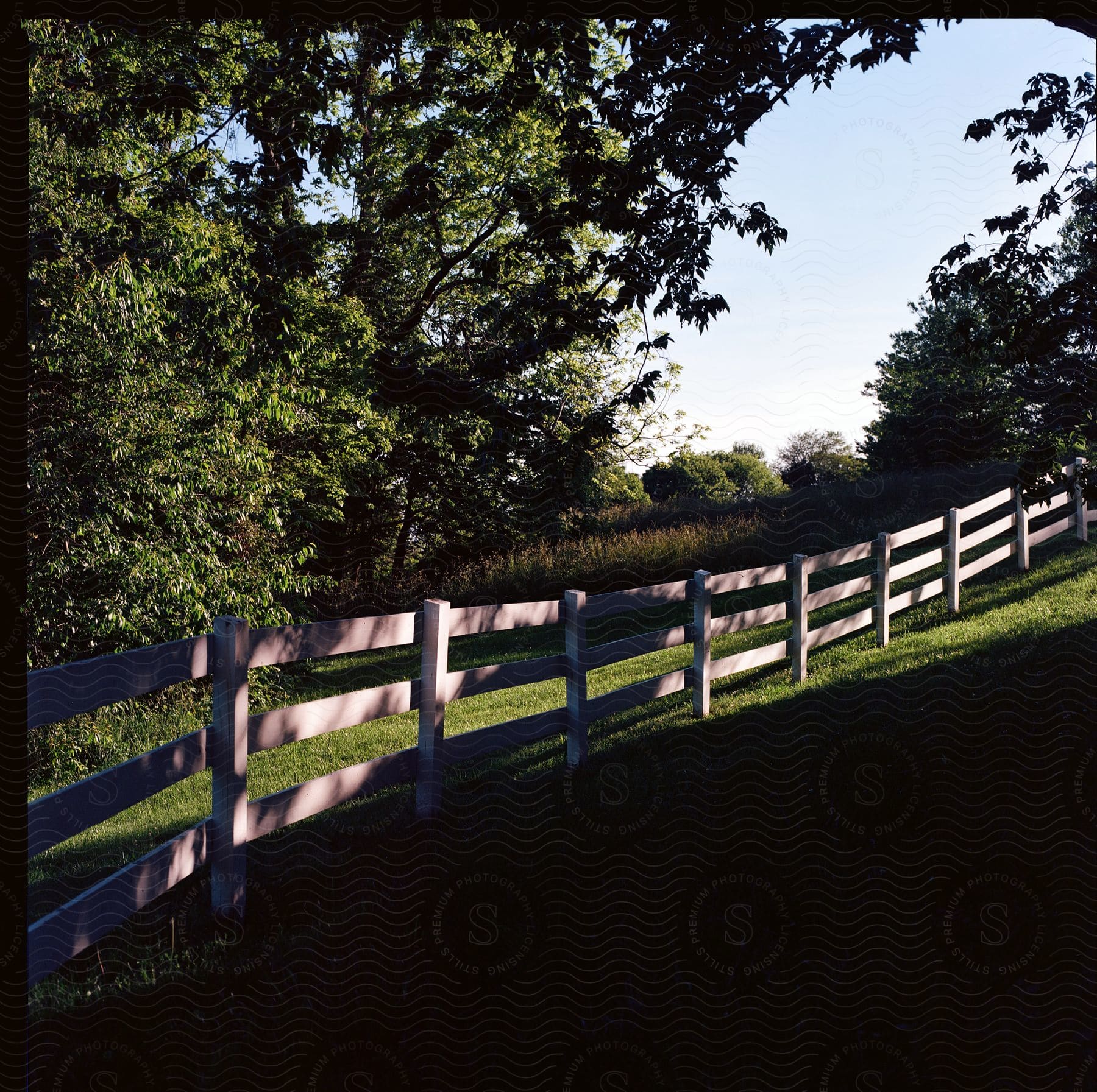 Sunlight and shadow on a wooden fence going up a lush green slope in the farm land of virginia