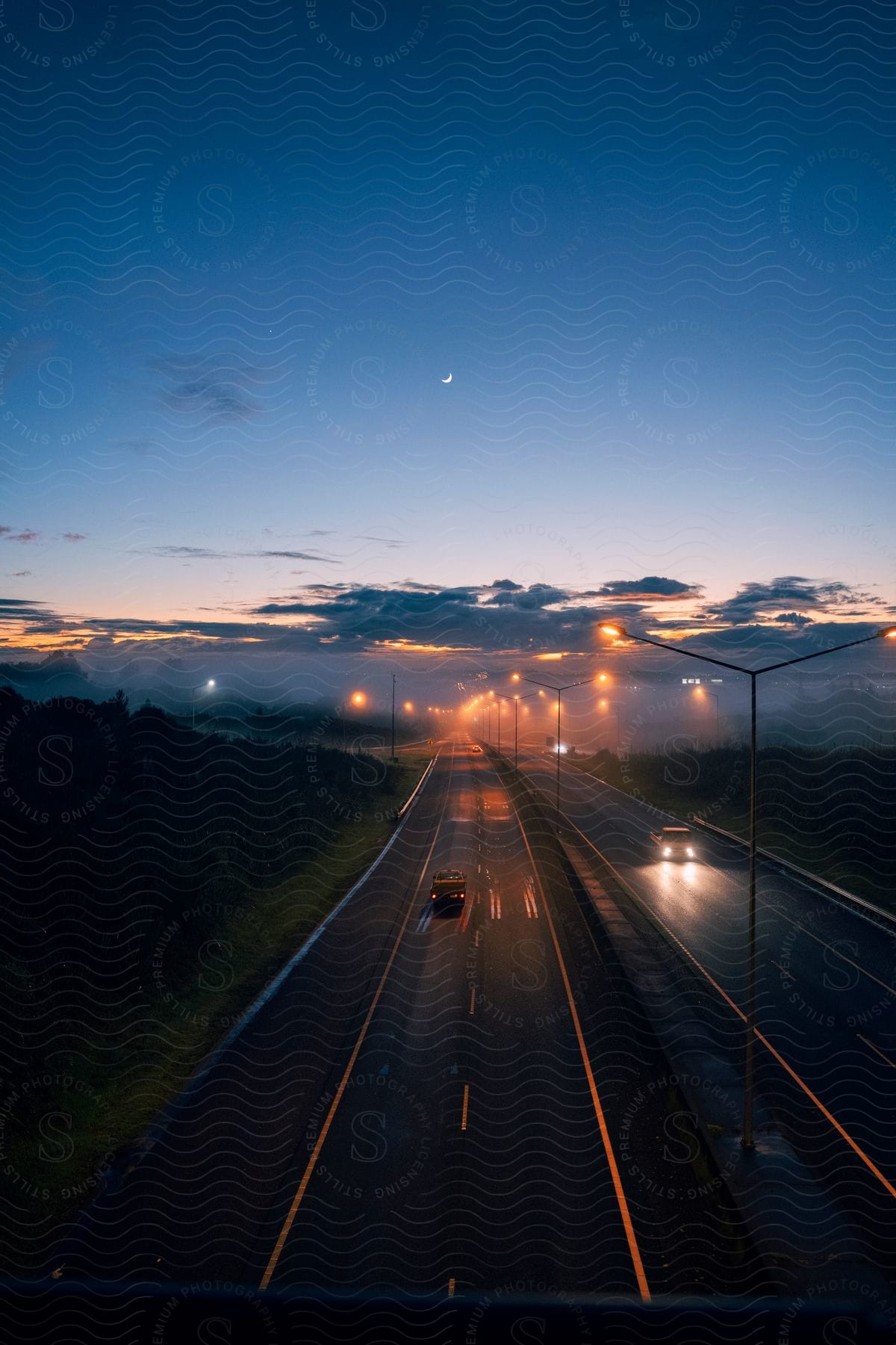 A deserted road at dusk with a car driving on the asphalt under a colorful sky