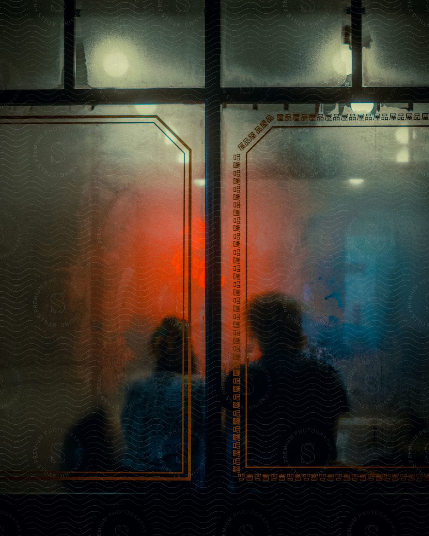 A woman stands near a window adorned with a rectangular painting in a dimly lit interior space