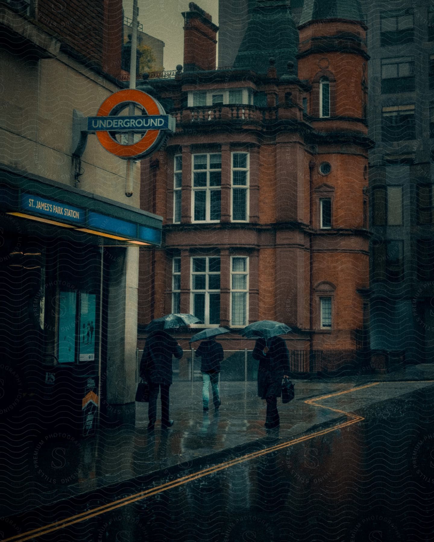 People walking with umbrellas on a rainy city street near a subway station entrance