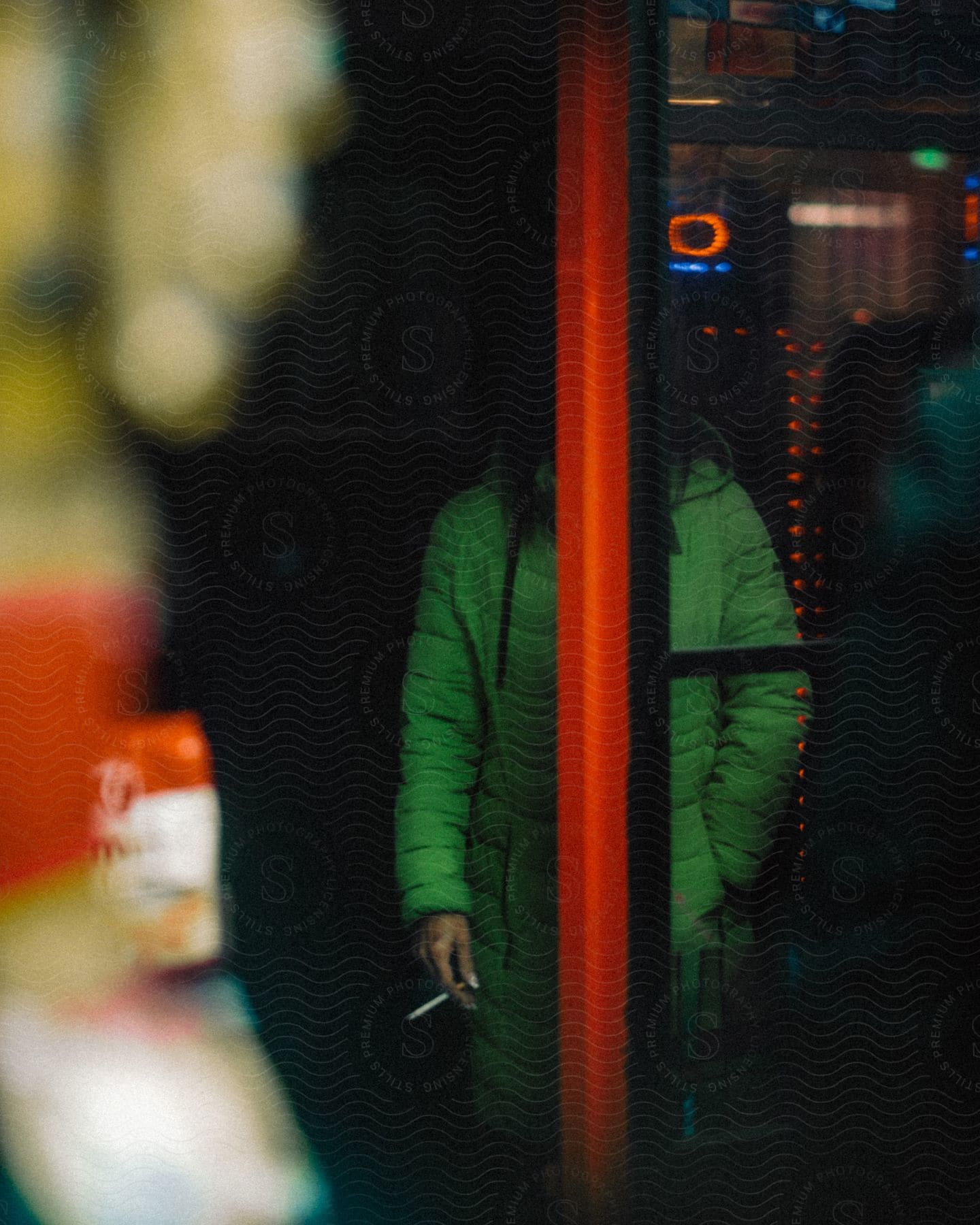 An individual wearing a green jacket holds a cigarette at night