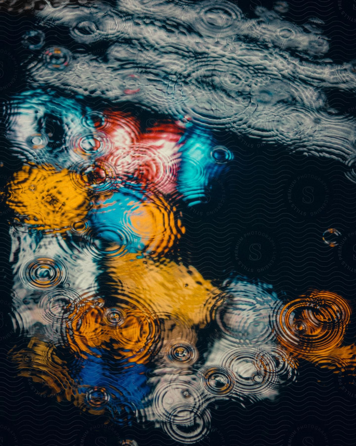 Bright store lights reflected in a rain puddle with raindrop ripples