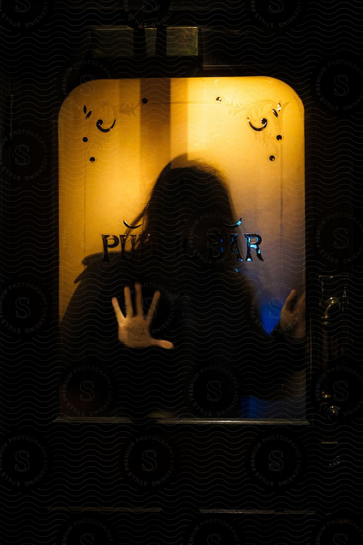 Stock photo of silhouette of a young woman behind a glass door under amber lights