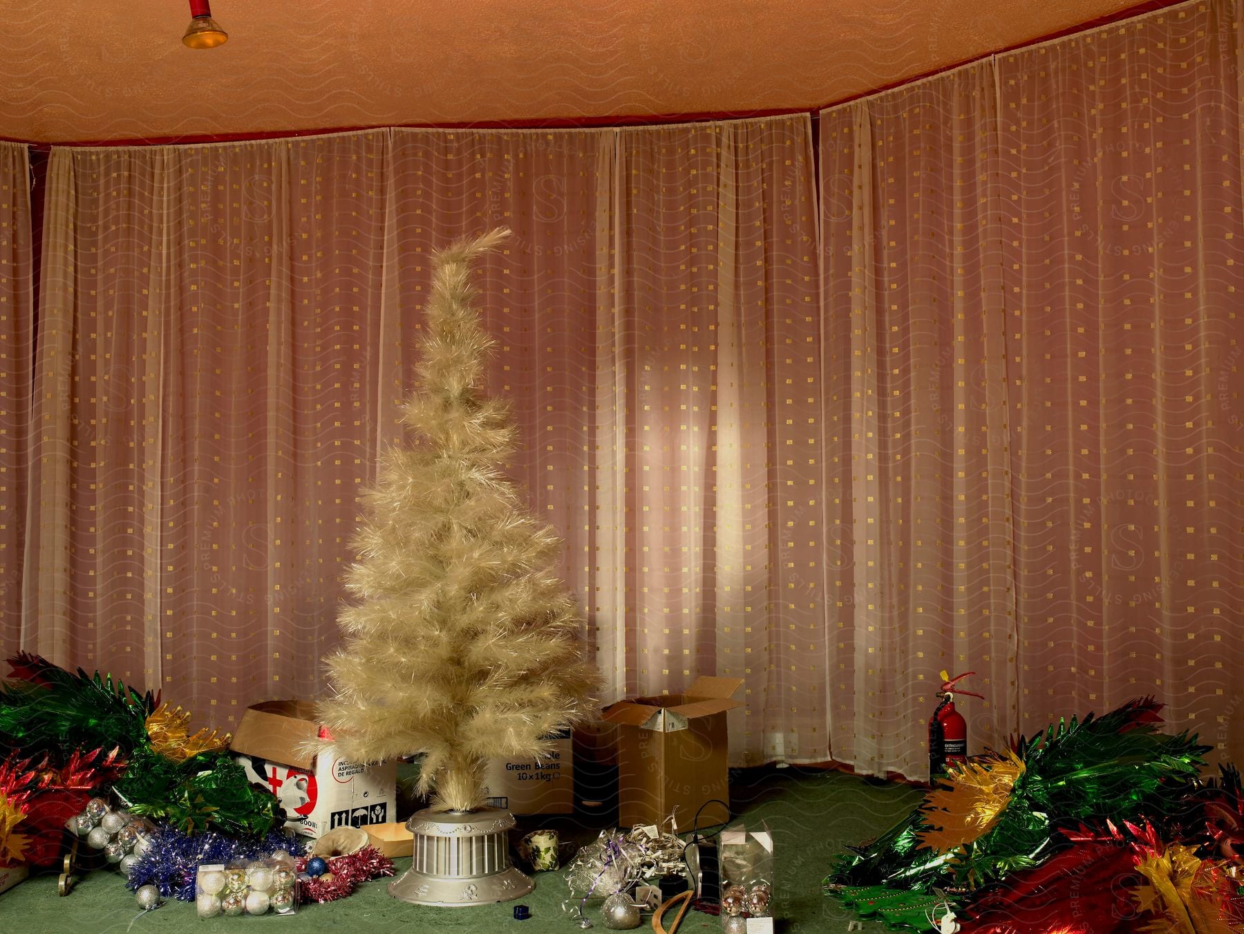 A golden christmas tree with various decorations stands in front of large curtains in a room