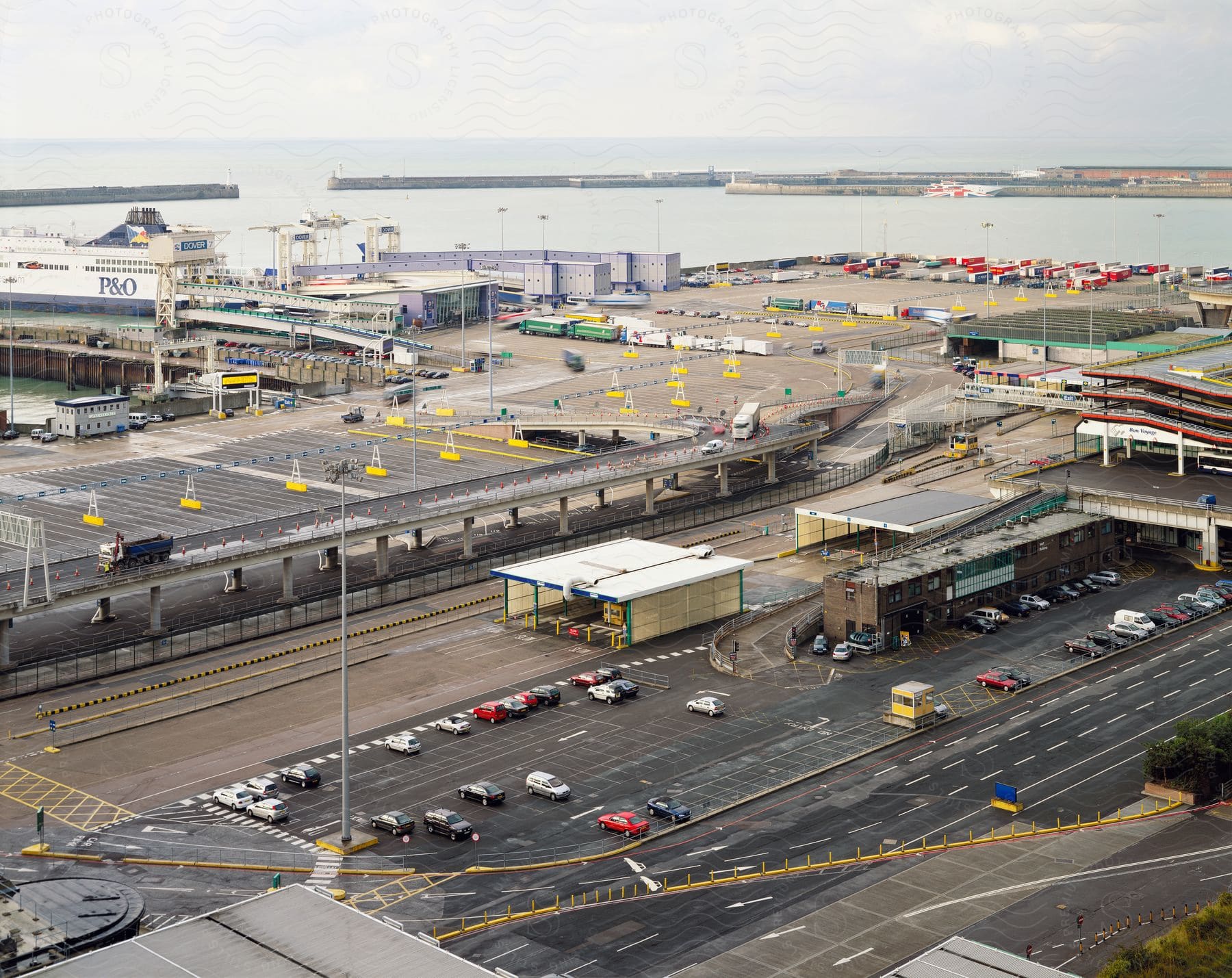 Aerial view of a port with a large cruise ship docked and semi trailers and cars in the port parking lots