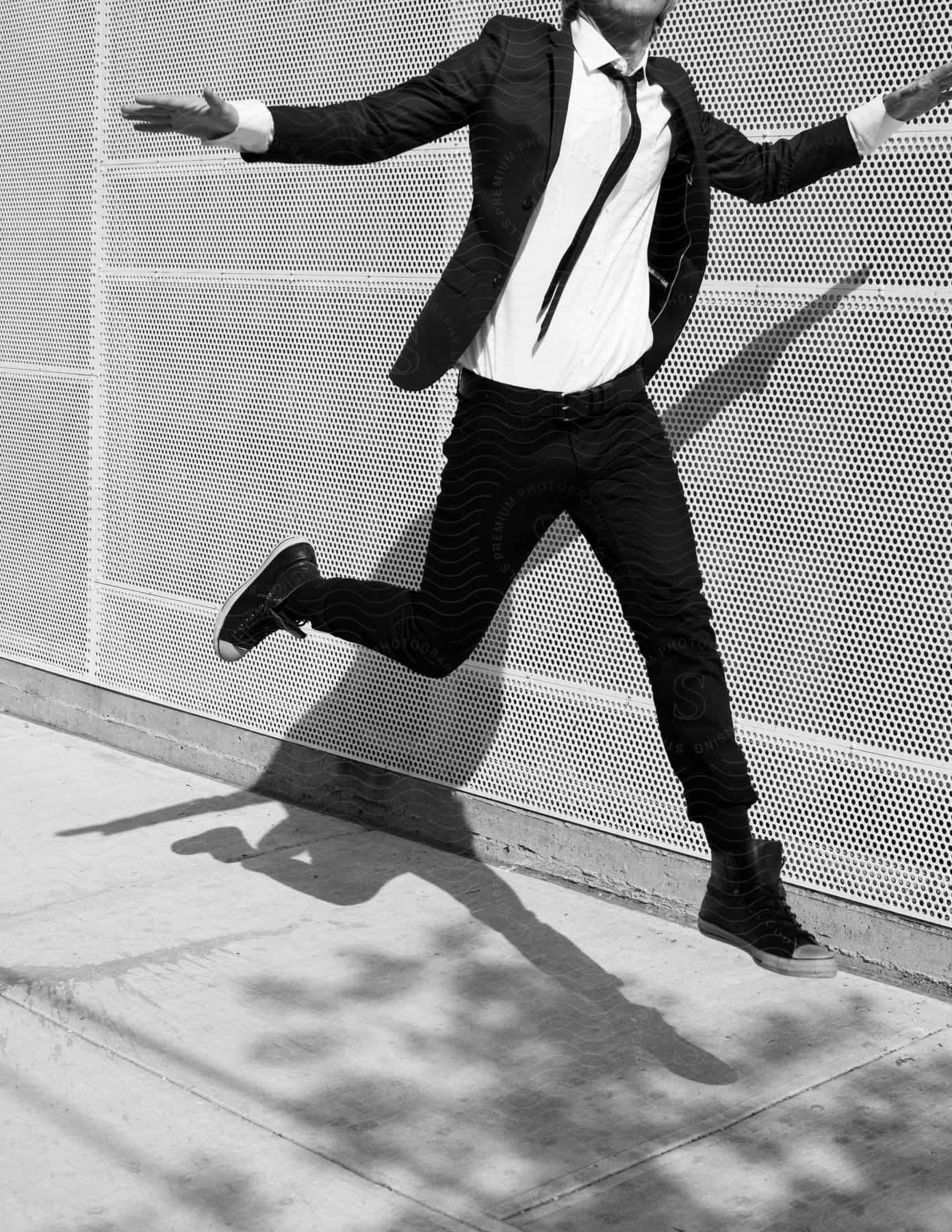 A man wearing a suit jumps on the sidewalk outdoors