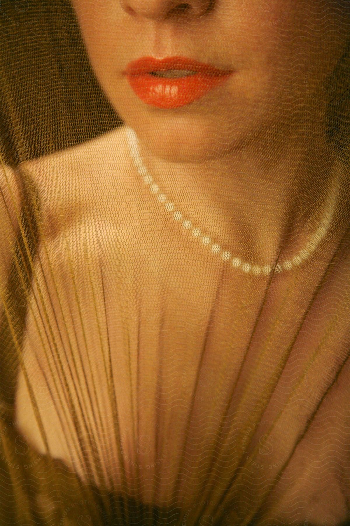 Elegant woman wearing a pearl necklace and red lipstick seen behind a veil