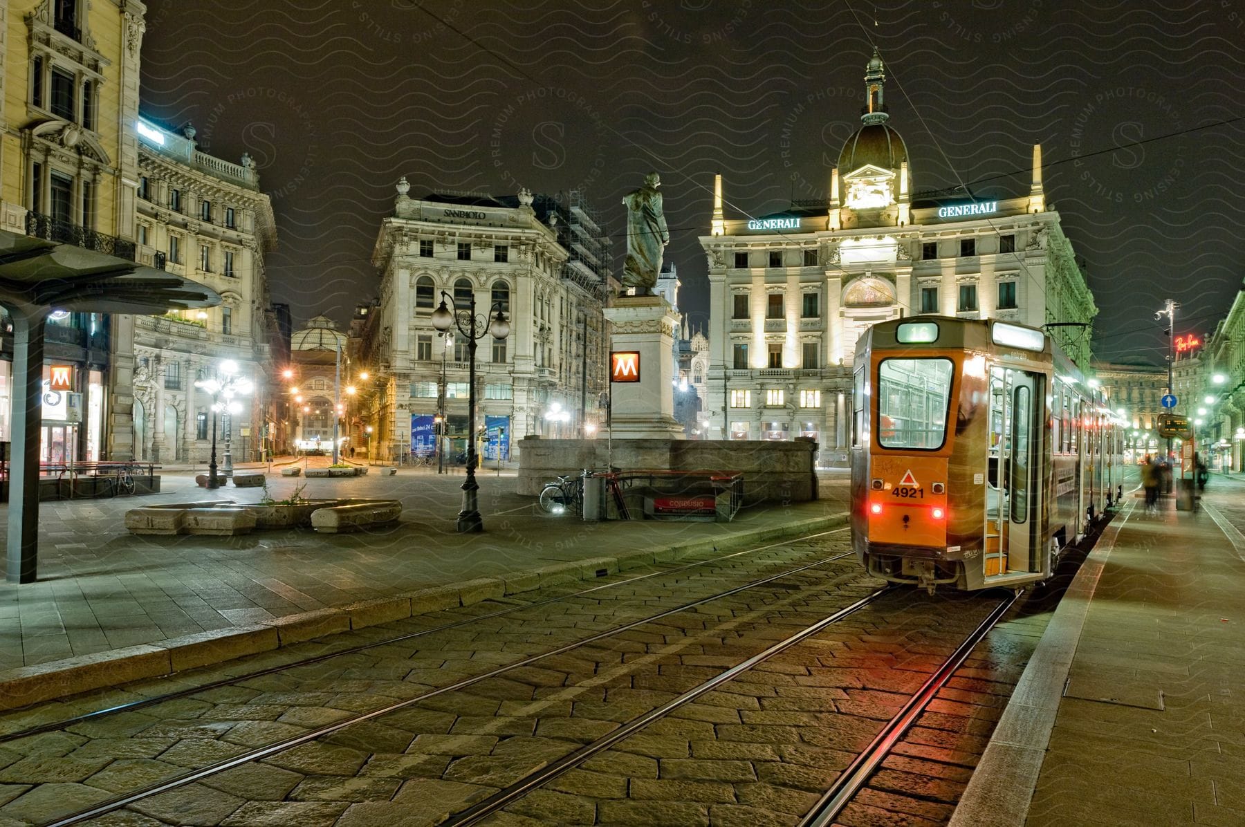 An electric rail bus passes through a welllit street at night surrounded by buildings creating a vibrant urban atmosphere