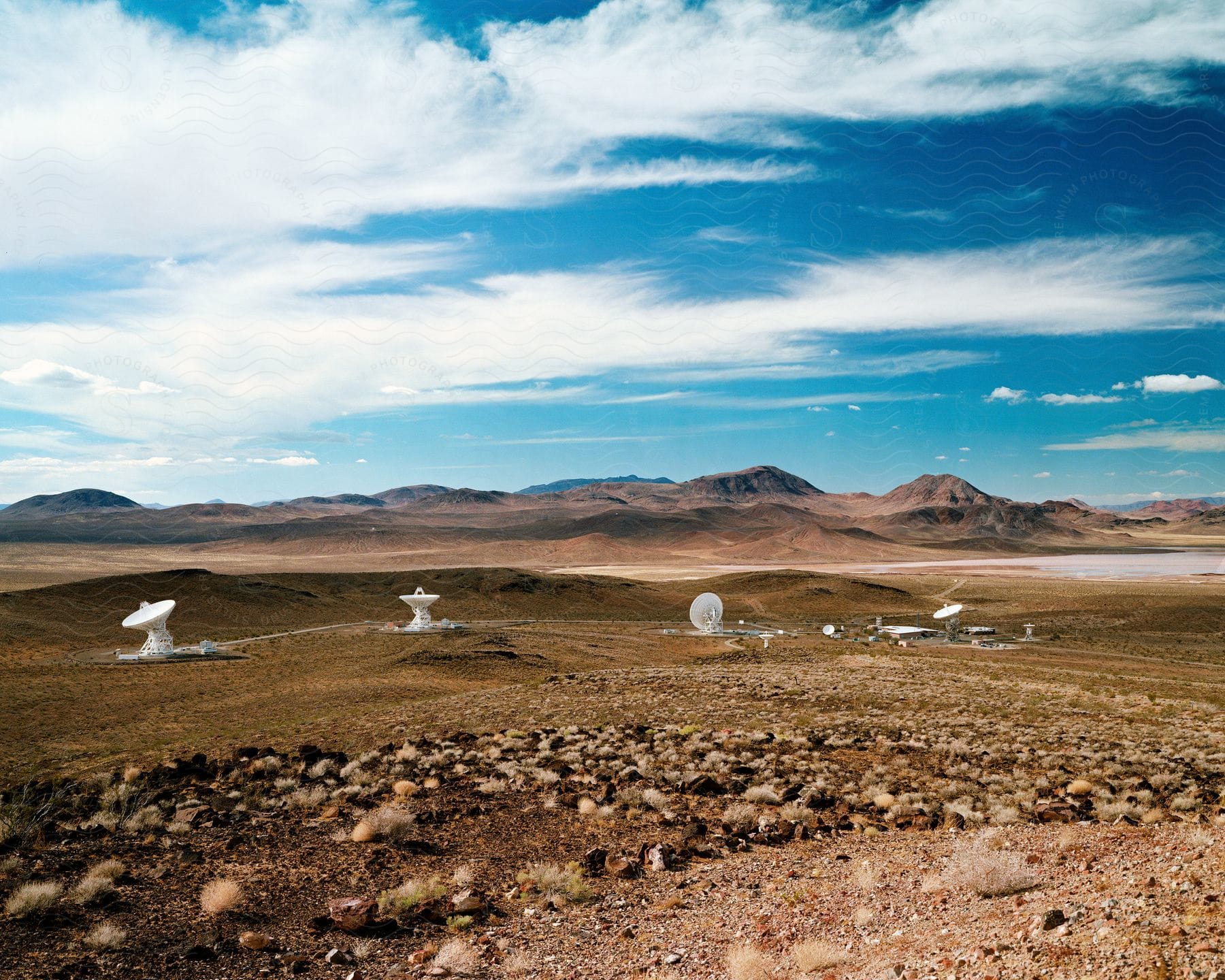 Satellite dishes on a grass plain with mountains in the background