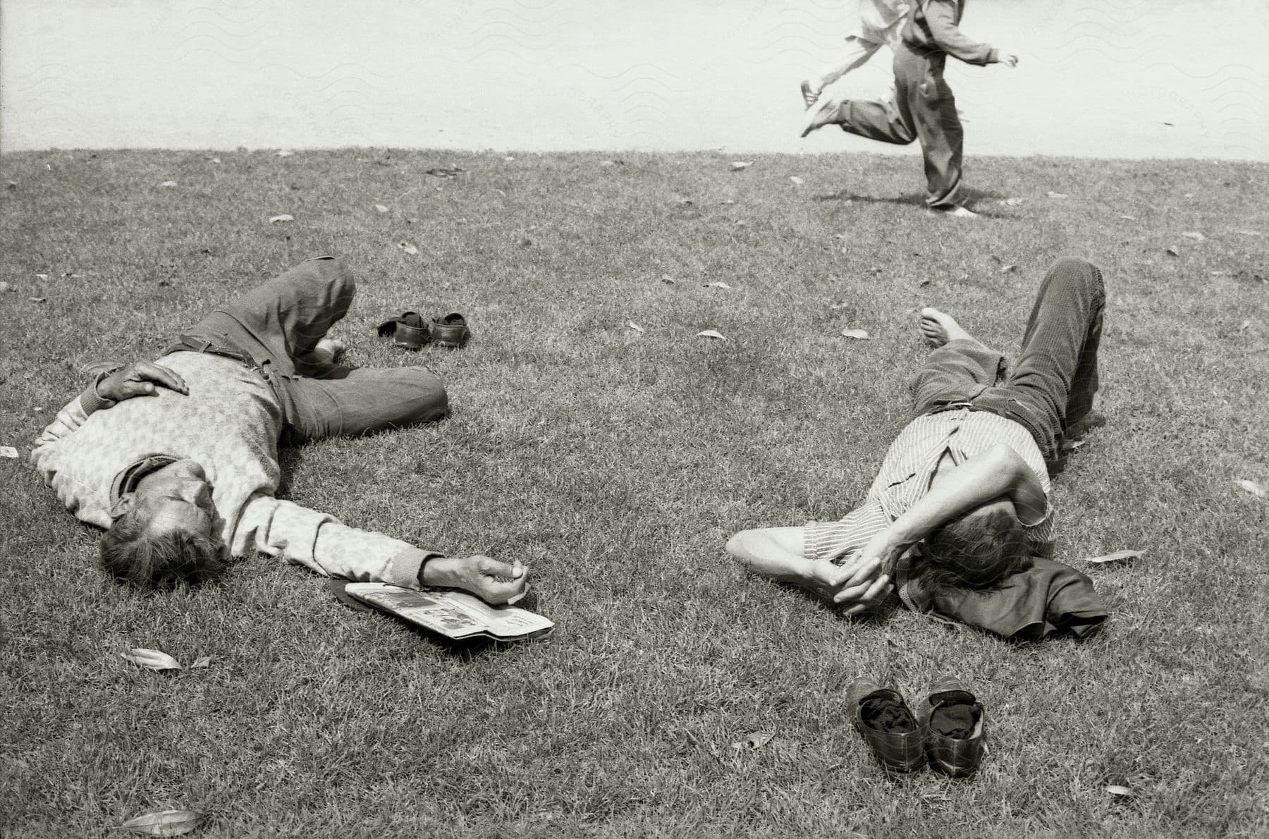 Two men resting on a grassy field appearing tired in a black and white image