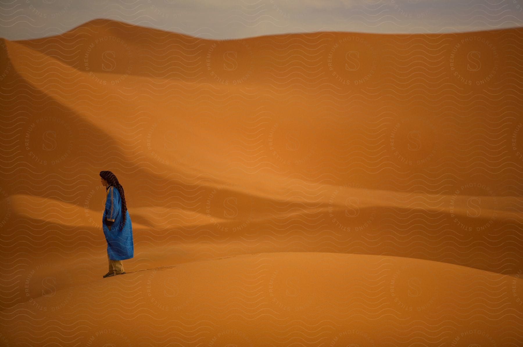 Man standing on yellow sand in the desert wearing a blue overcoat