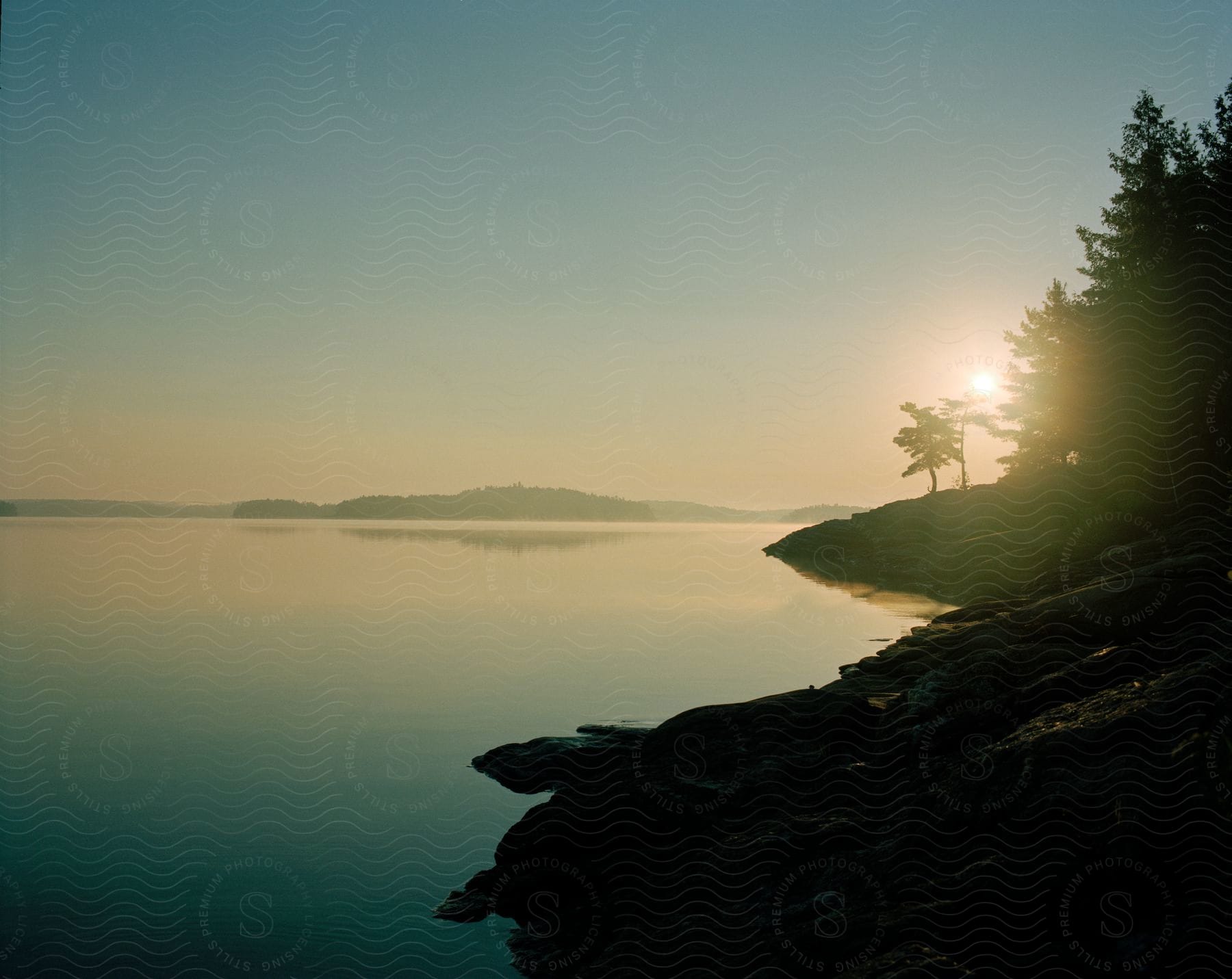 A sunset view of a lakes shoreline with rocks and trees