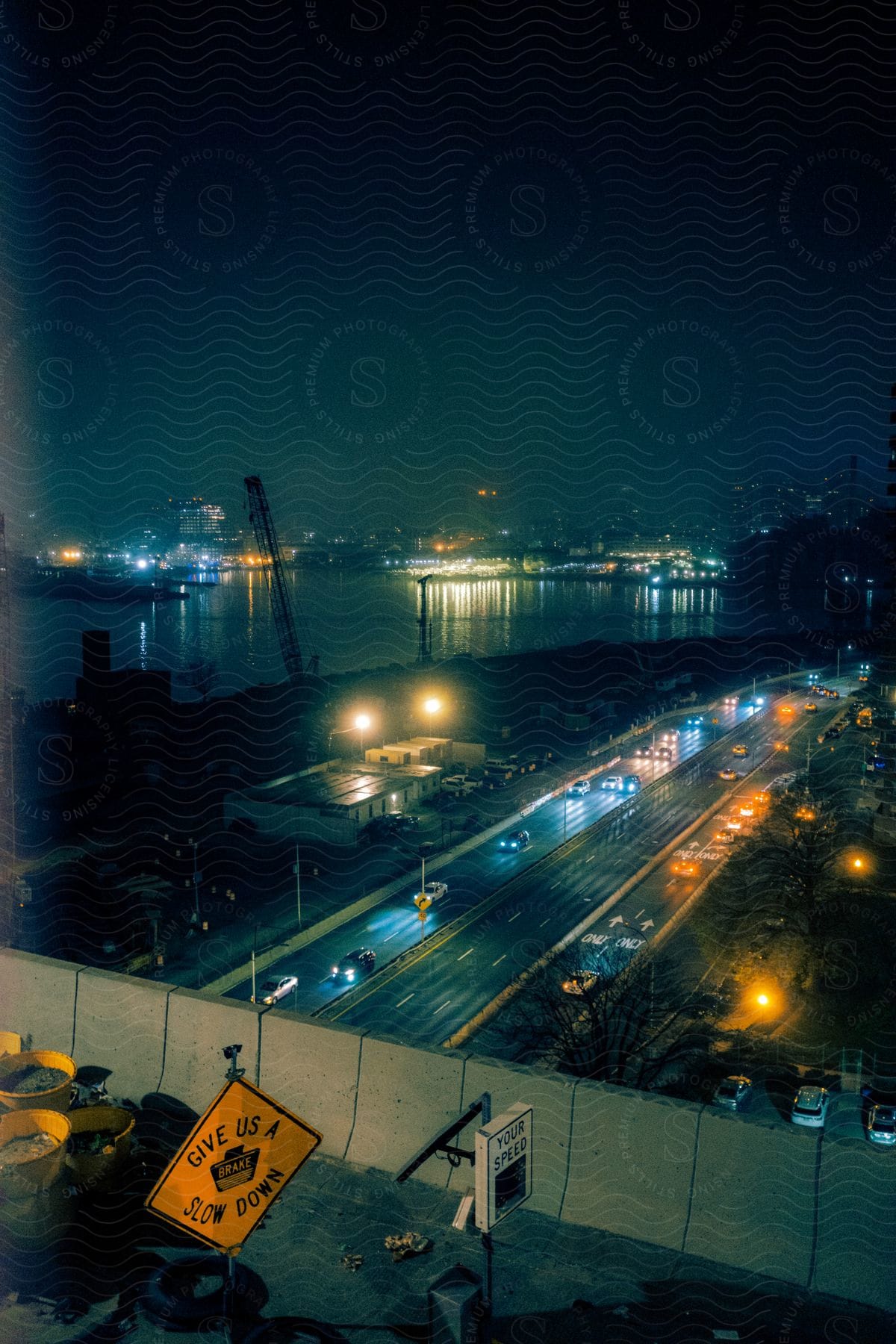 Busy highway at night near the shoreline with a construction site and cranes casting faint light amidst traffic flow