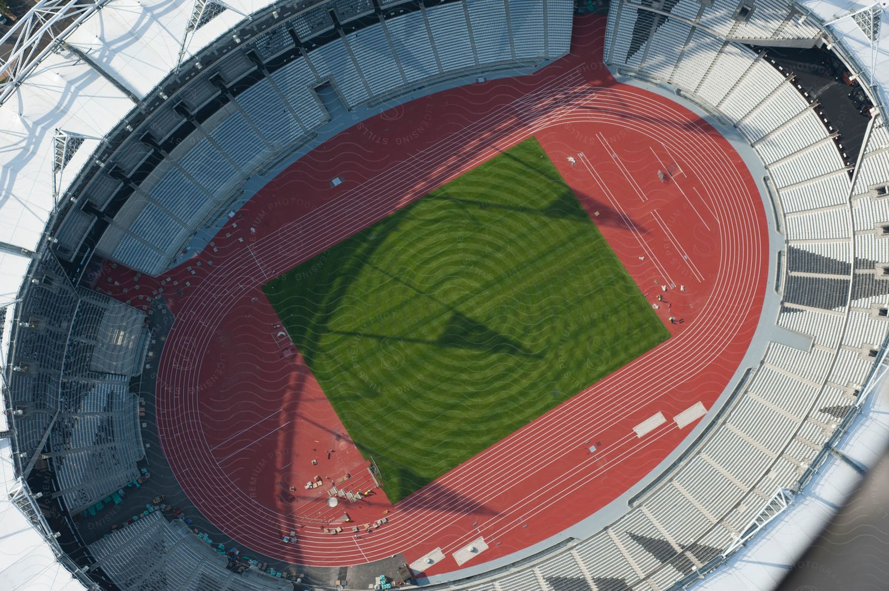 Aerial view of a massive white olympic stadium with a burnt red race track and a perfectly mowed green turf lawn