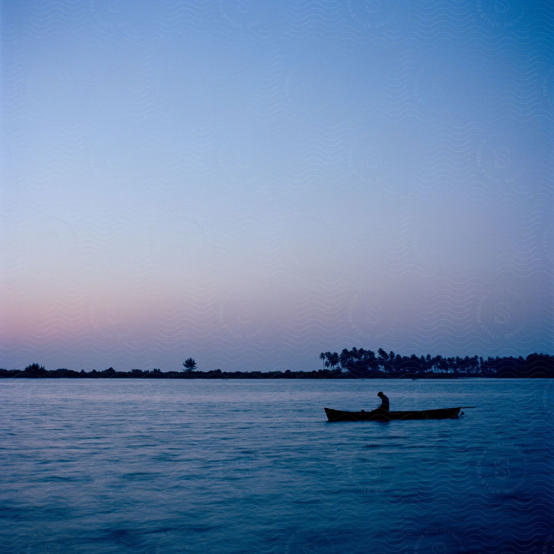 A silhouette of a person sitting on a boat above water at dusk