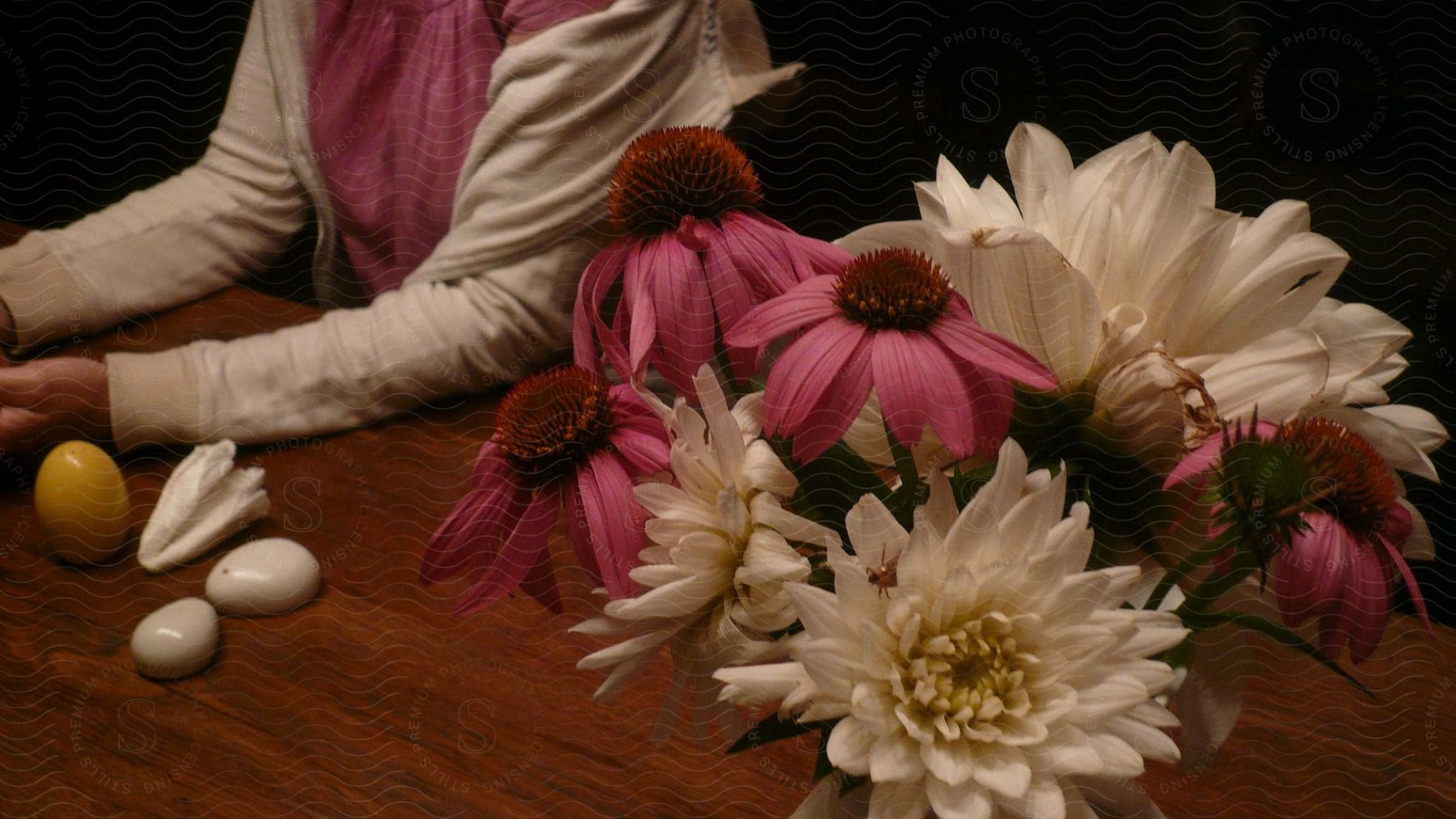 A woman sits next to a bouquet of flowers indoors on a tabletop