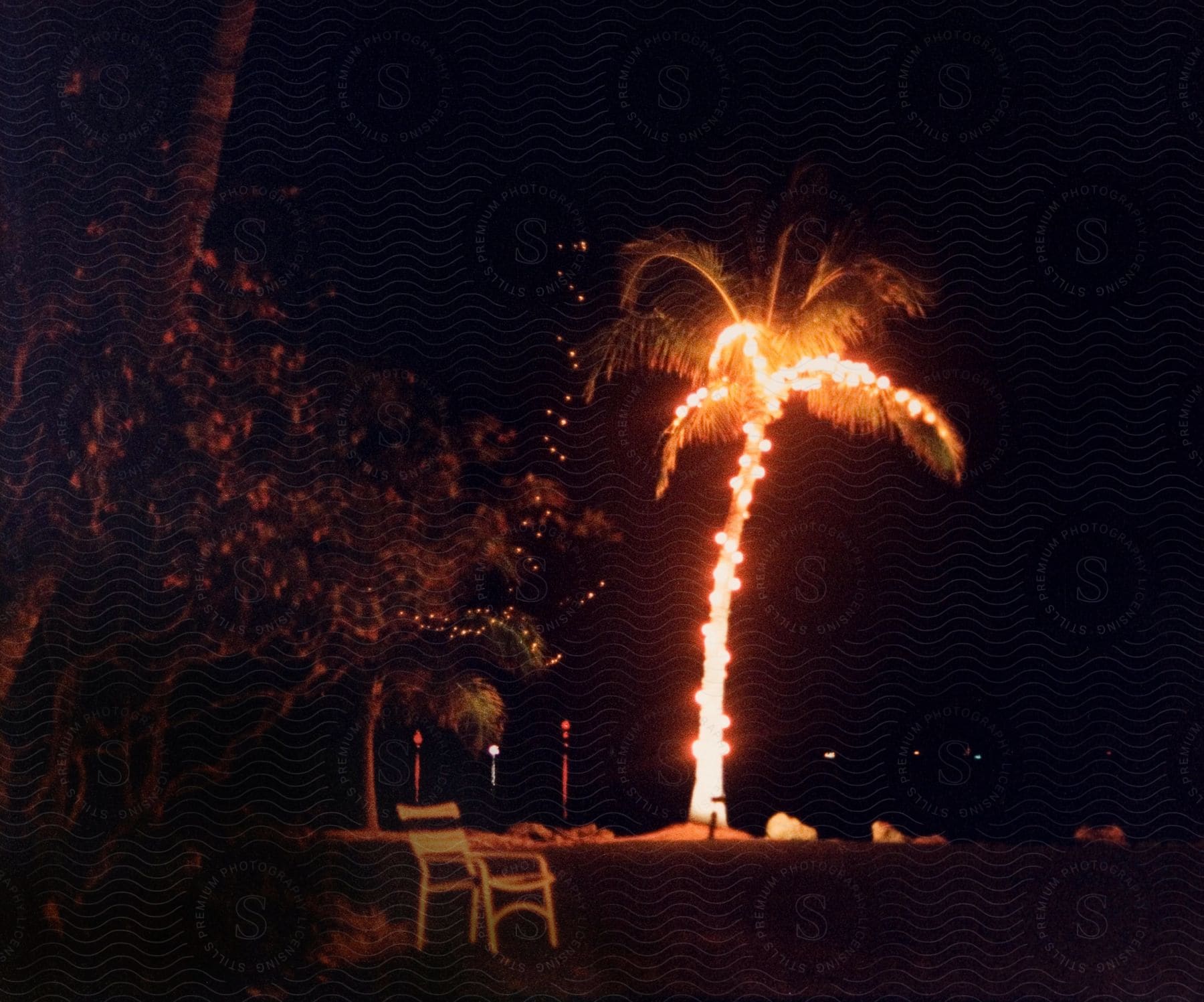 A brightly lit palm tree adorned with christmas lights next to a lawn chair