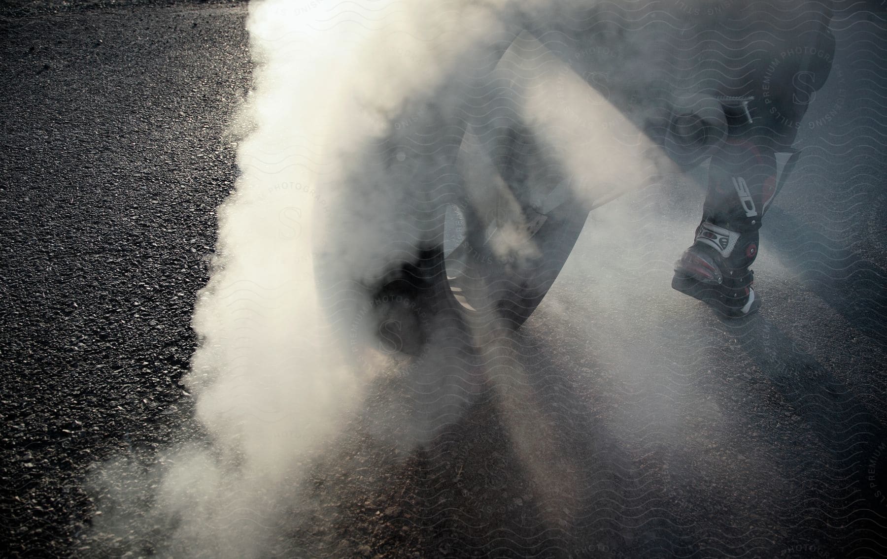 A closeup of a persons feet on a motorcycle as the tire smokes