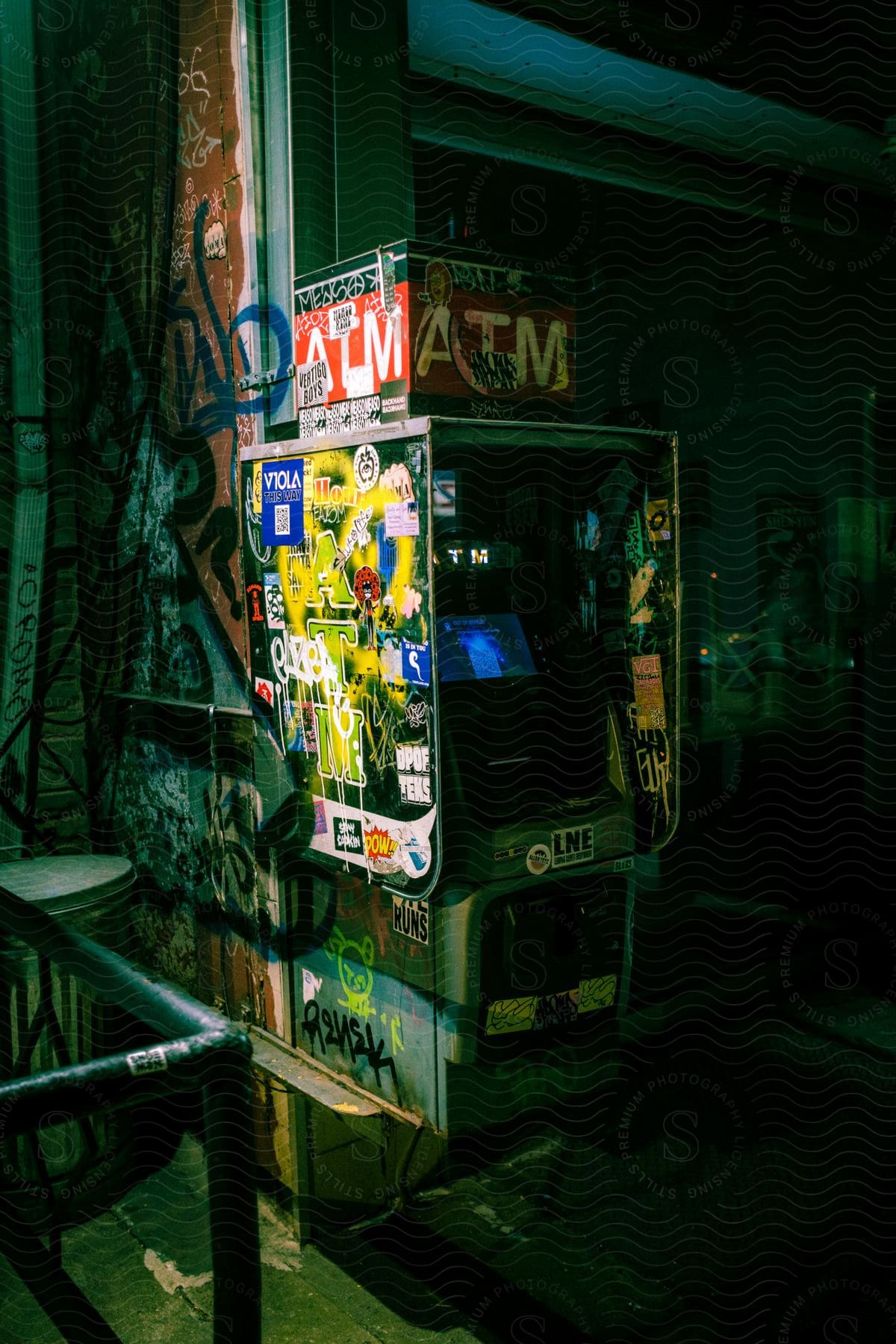 Atm machine covered in stickers and graffiti on a city corner at night