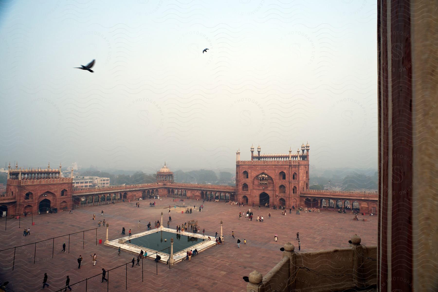 A large courtyard with old architecture has tourists visiting on an overcast and foggy day