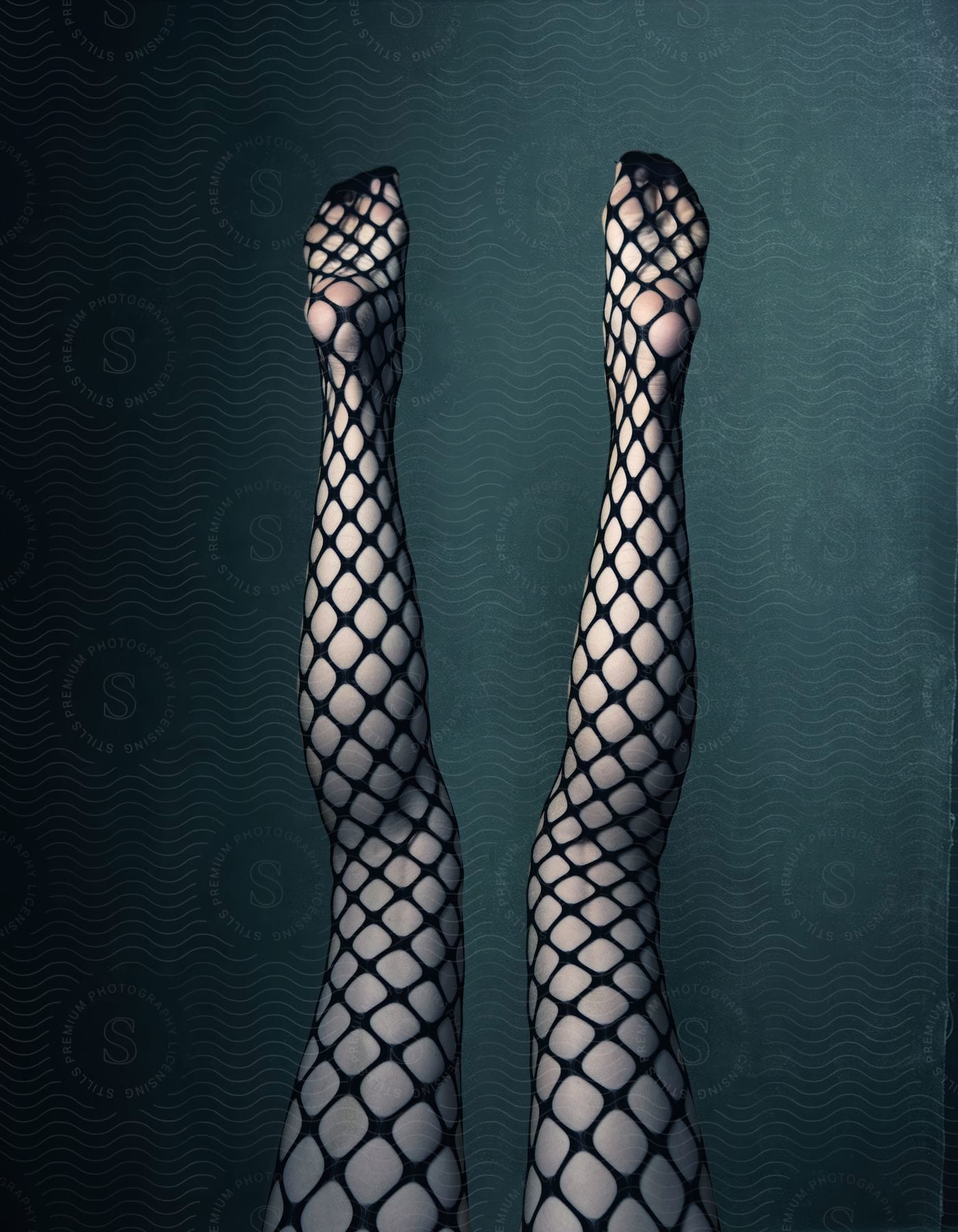 A womans legs with net stockings are in the air in front of a plain grey background