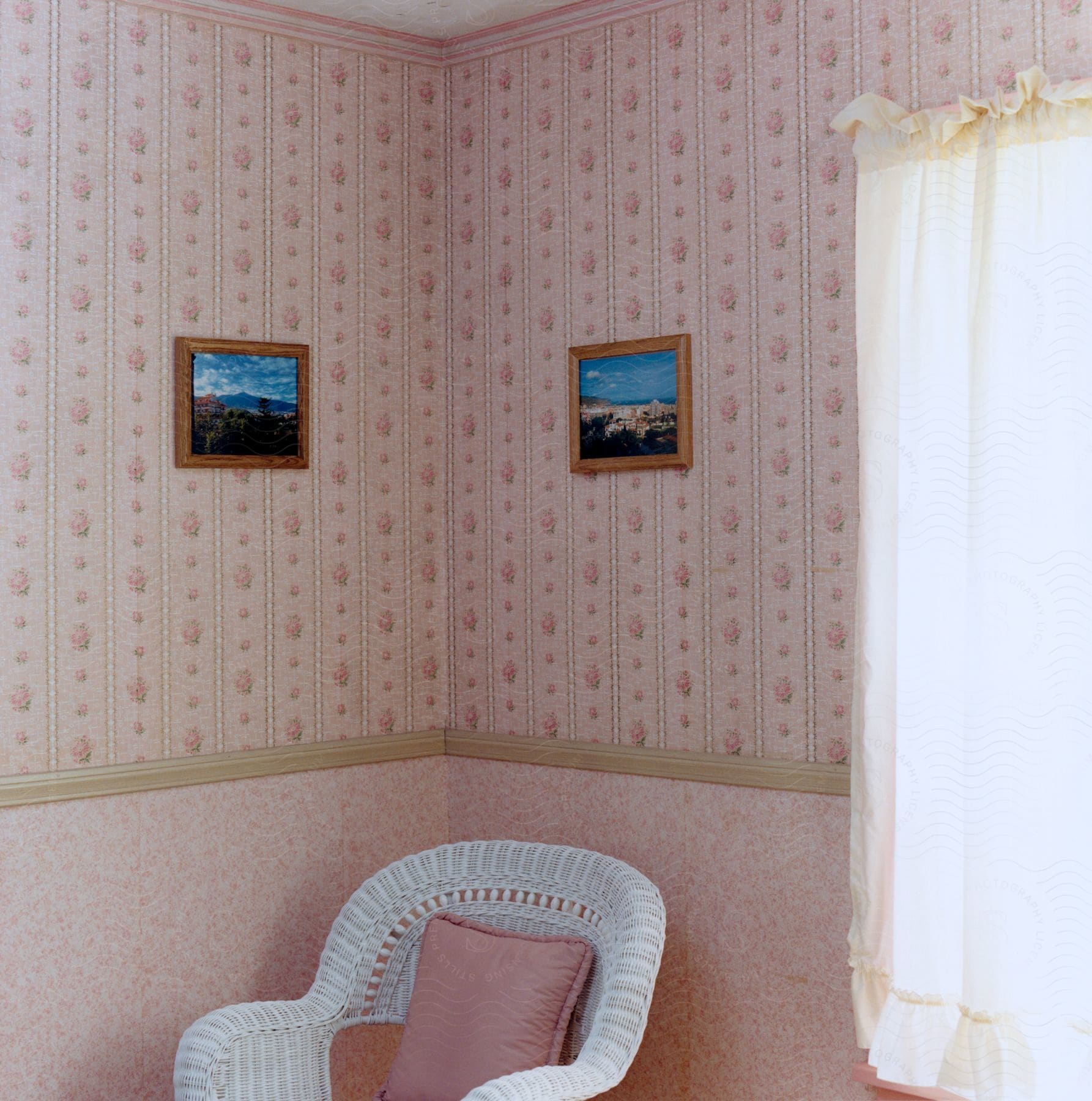 A pink and white room with white curtains a wicker chair and pink throw pillow and wallpaper