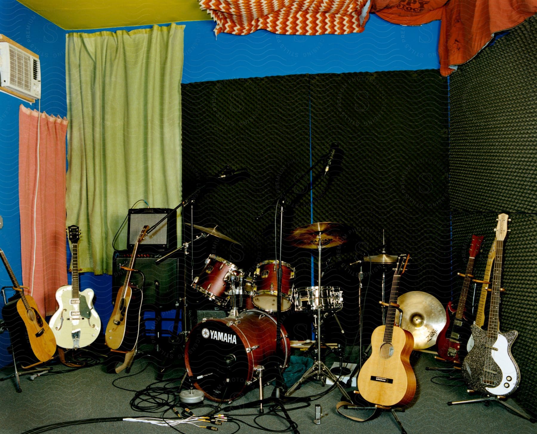 A drum set and guitars are set up on a small stage with amplifiers and musical equipment