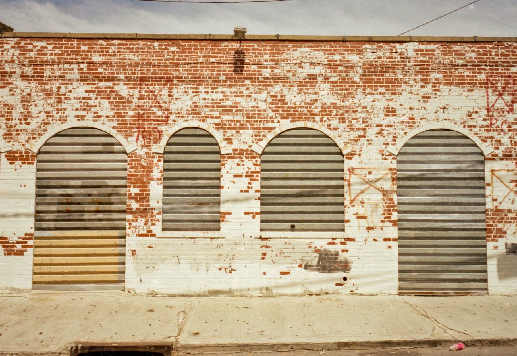 An old brick building with boarded up windows and doors stands along a sidewalk