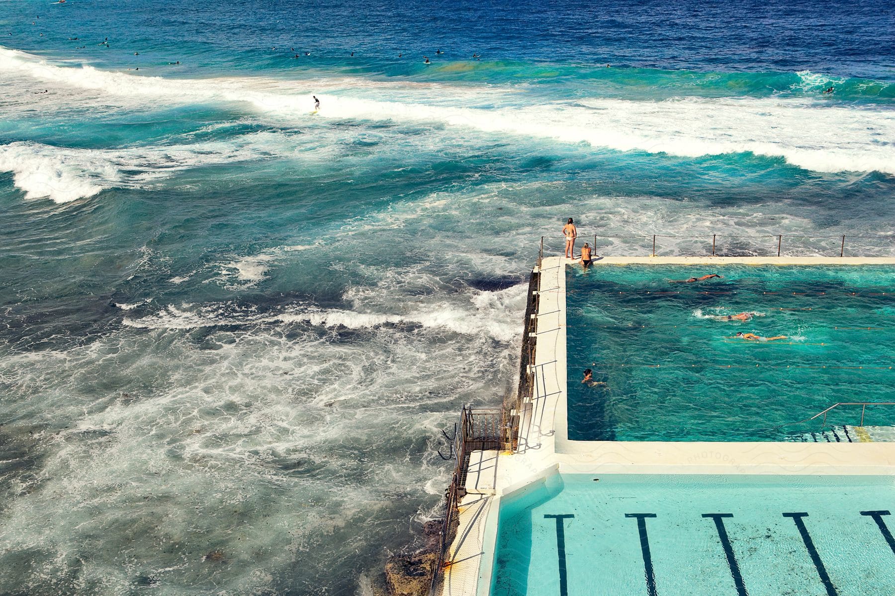 Oceanfront pools filled with people swimming and surfing in the sea on a sunny day