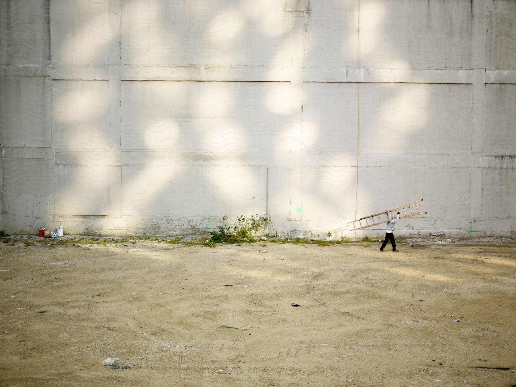 A man carrying a ladder walks along a concrete wall on a sunny day in chicago