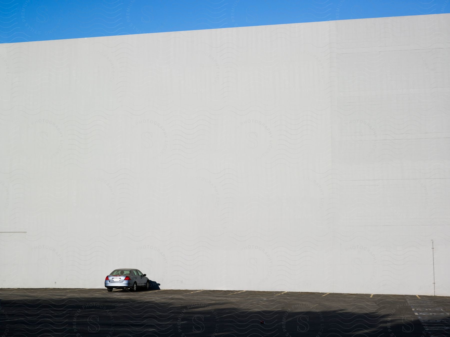 A silver car parked in a parking lot next to the grey wall of a large store