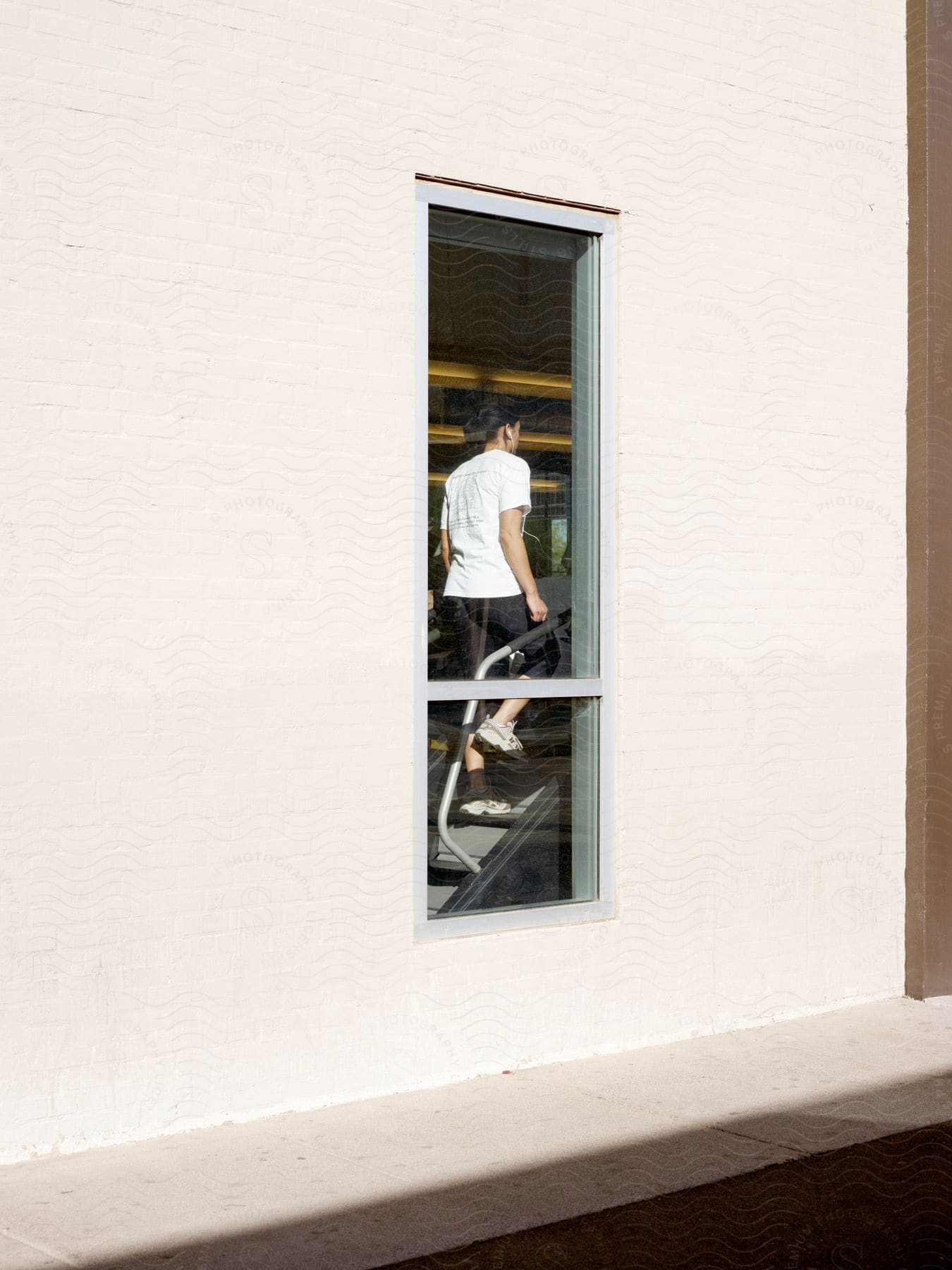 A woman exercising on a stair machine in a gym seen through a window