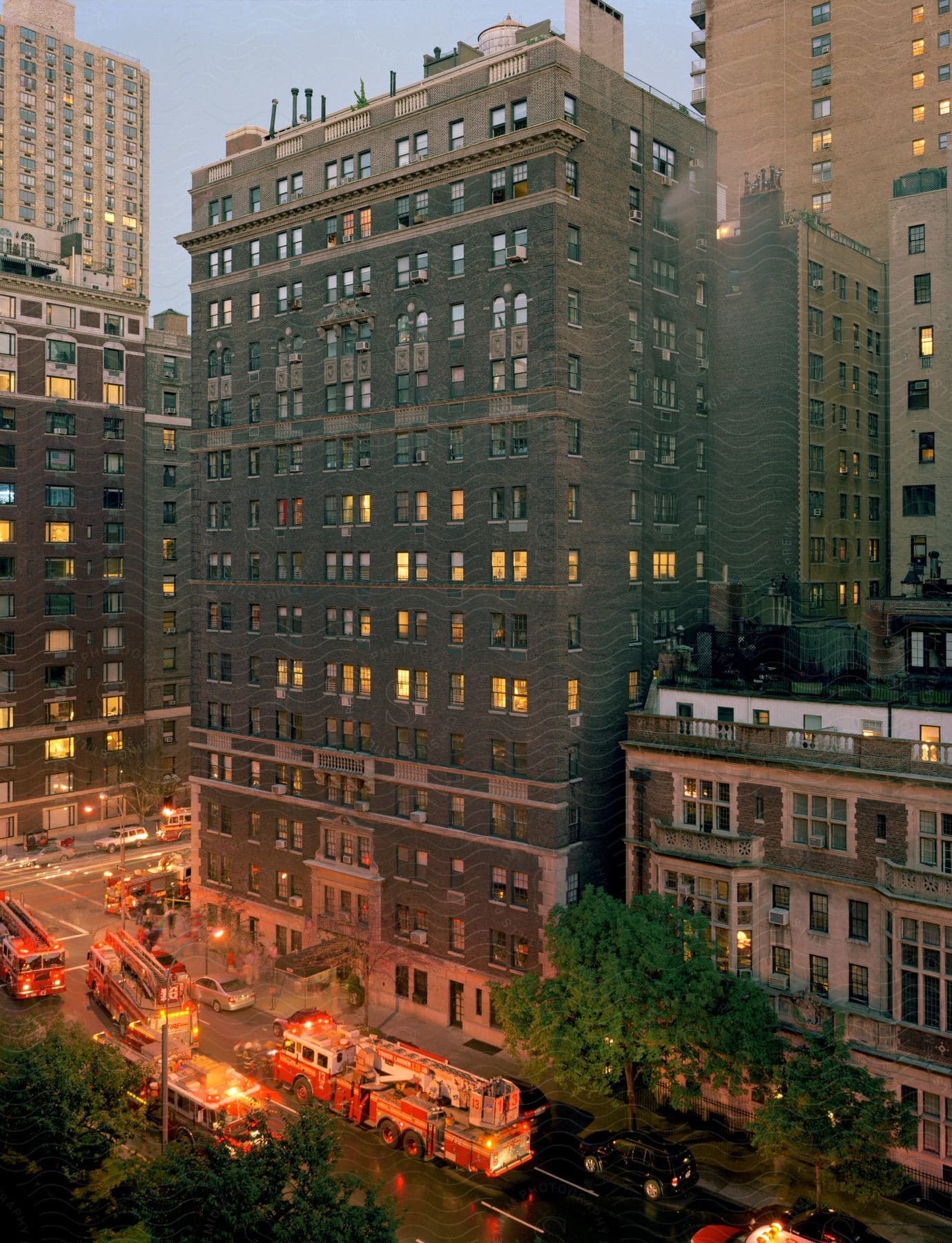 A grey brick highrise with smoke and firetrucks in front at dusk