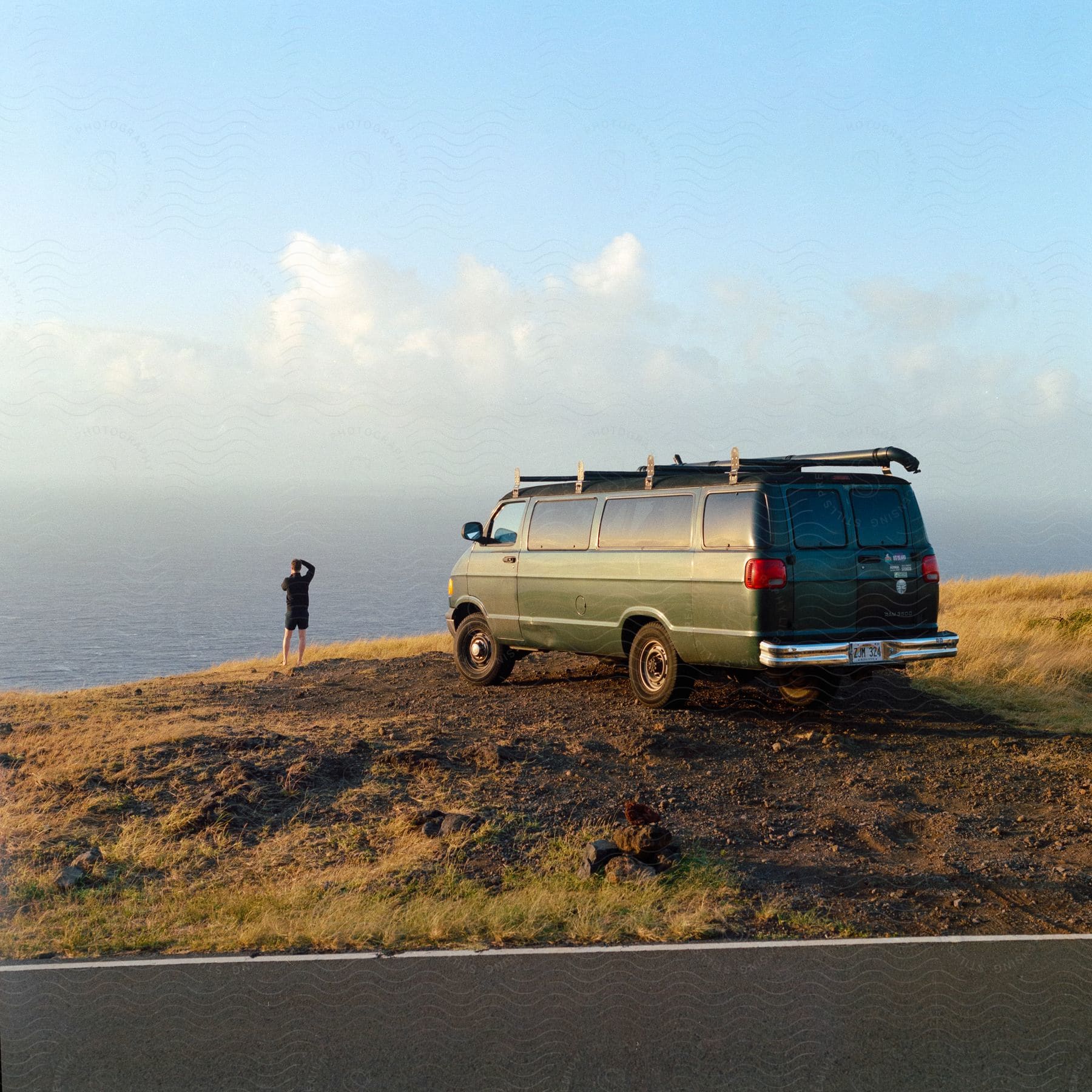 Man standing next to a green van overlooking water near shore during the day