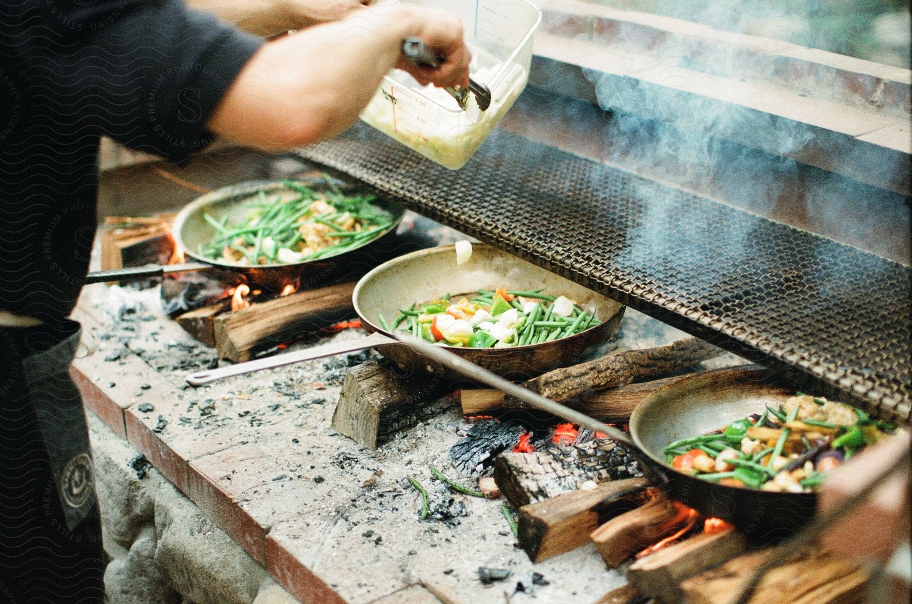 A person preparing healthy food on three different frying pans outdoors