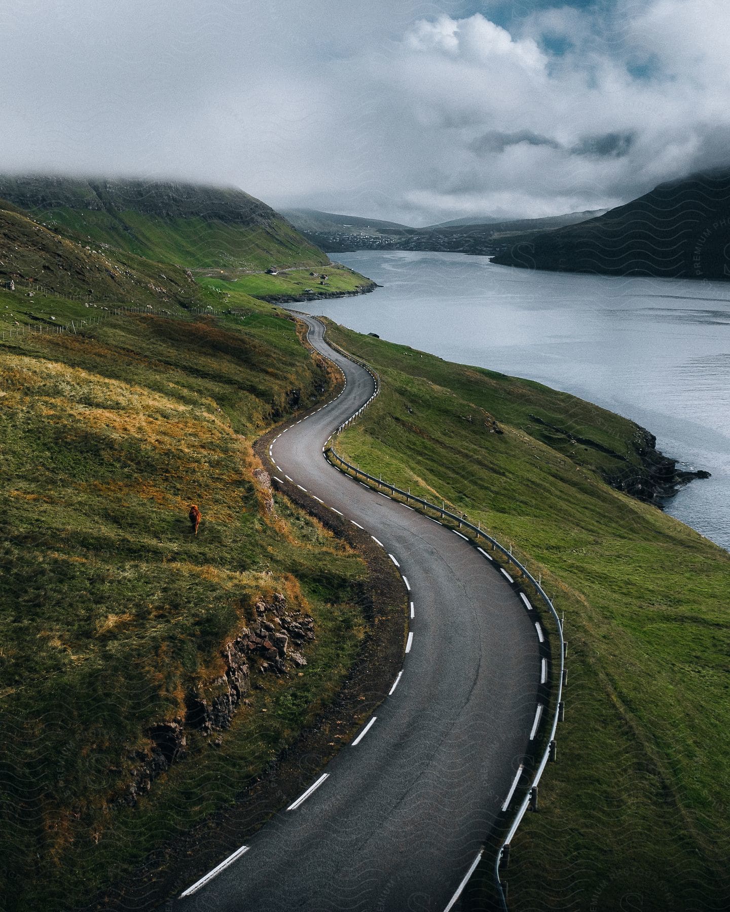 Road winding through hills near a river under cloudy skies