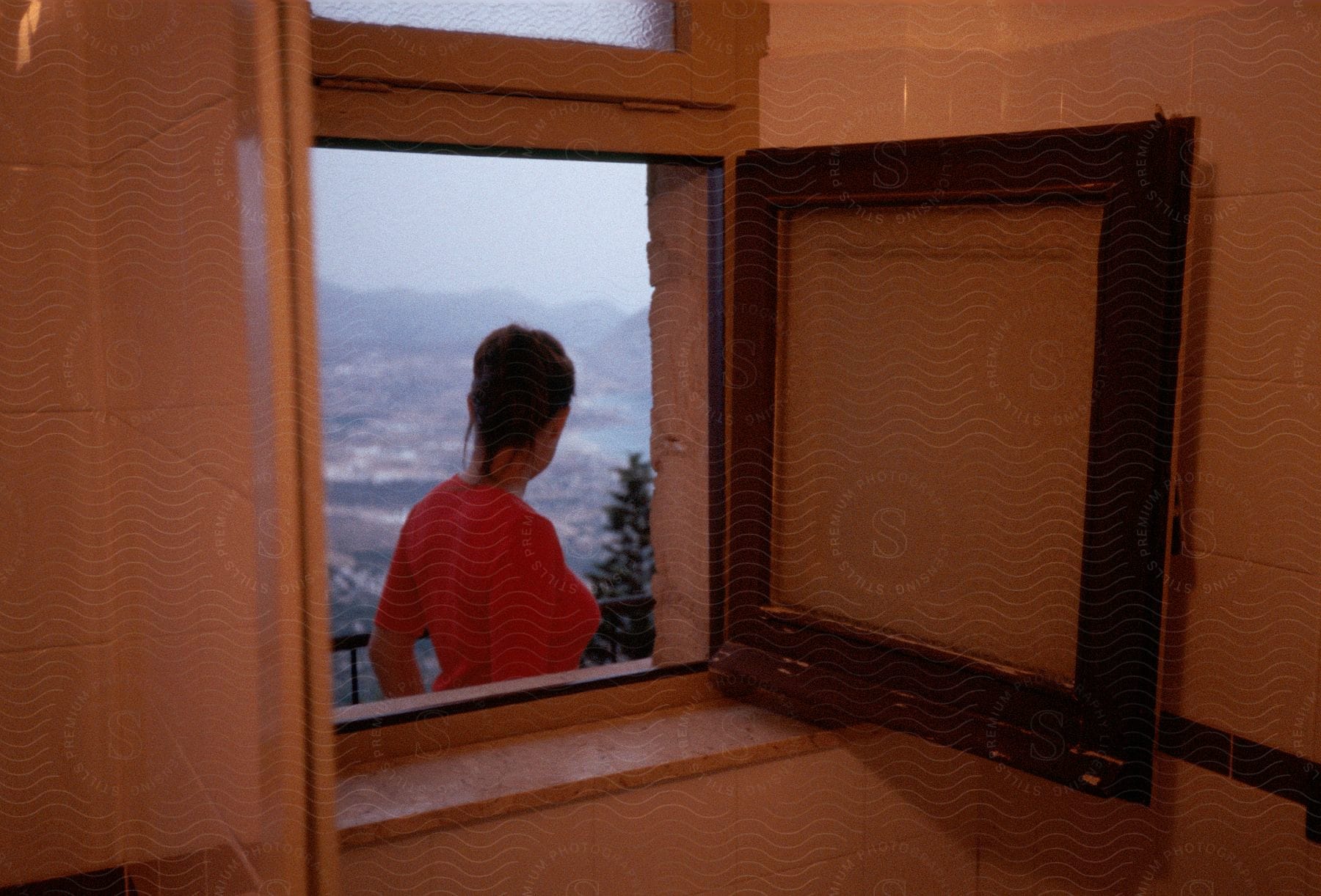 Woman standing on balcony looking at landscape through open bathroom window