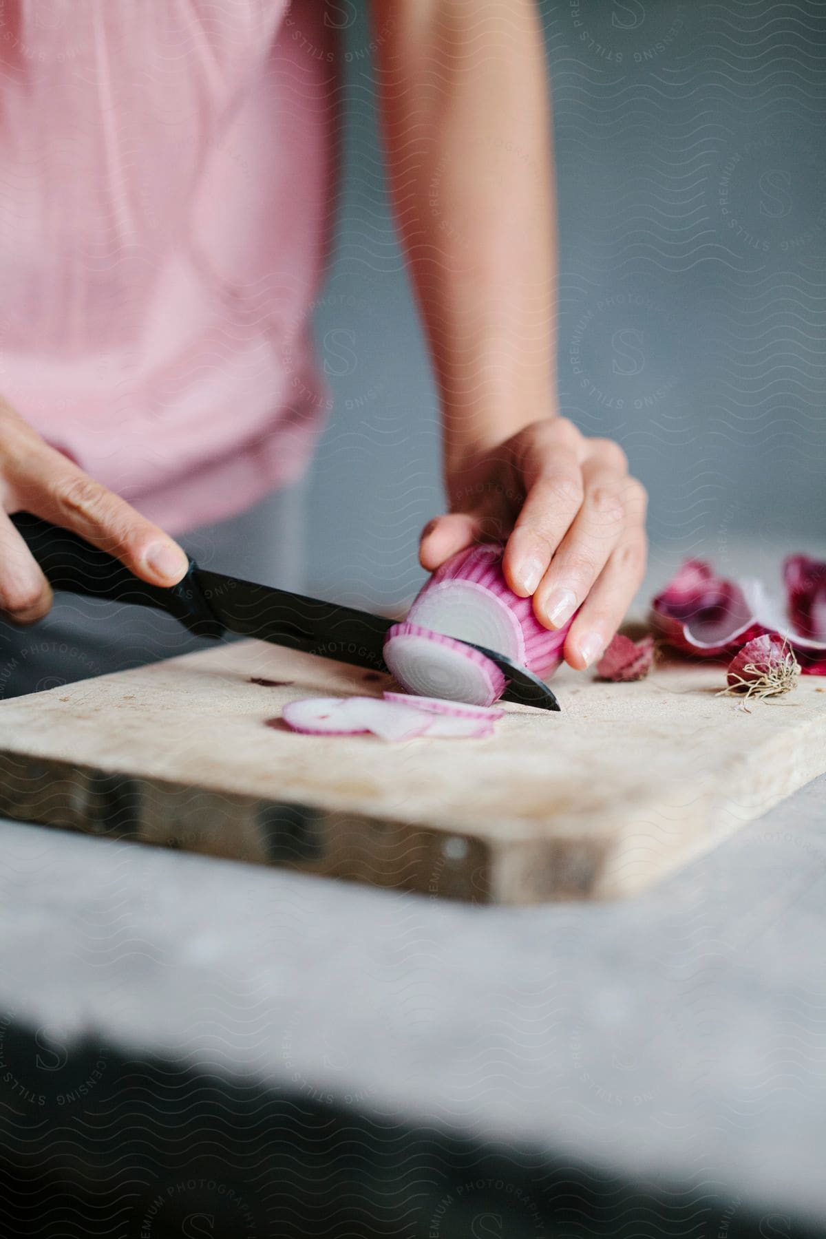 A pair of hands using a kitchen knife to cut a purple onion in a wooden chopping block