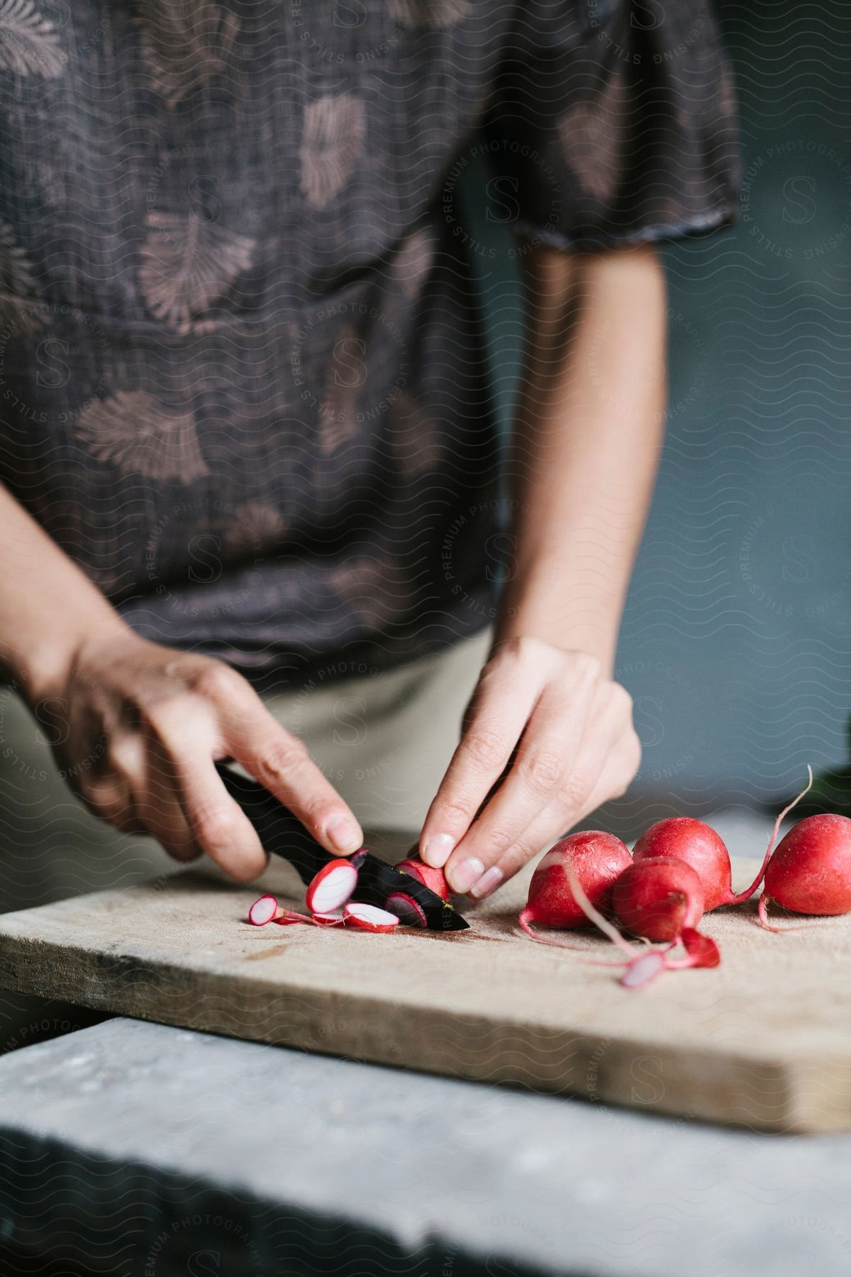 A person cuts radishes with a tiny knife on a cutting board