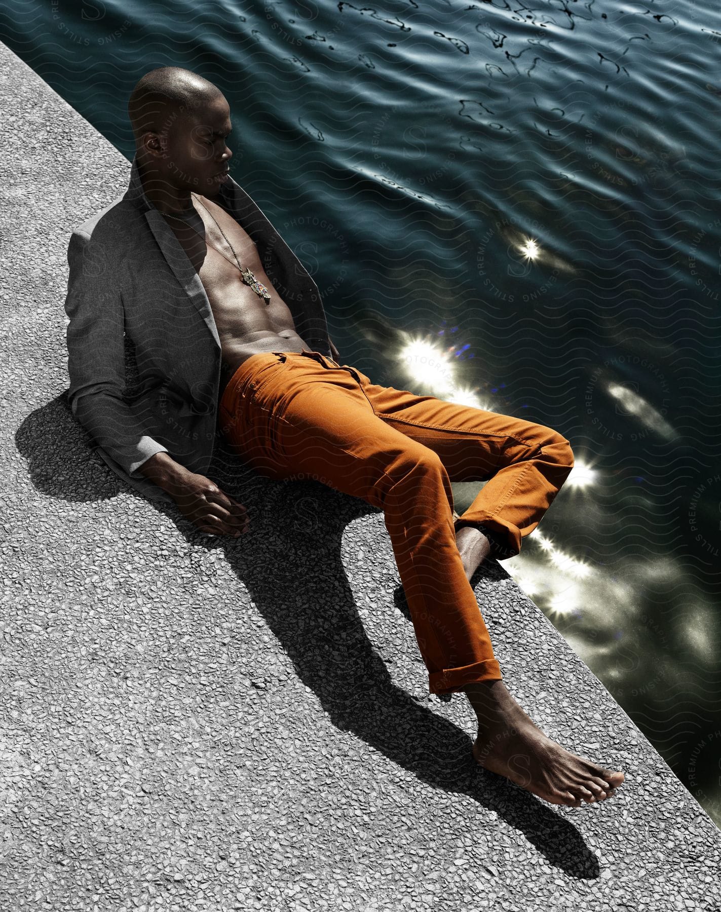 A male model posing for a photo on a sunny day next to water on a granite floor