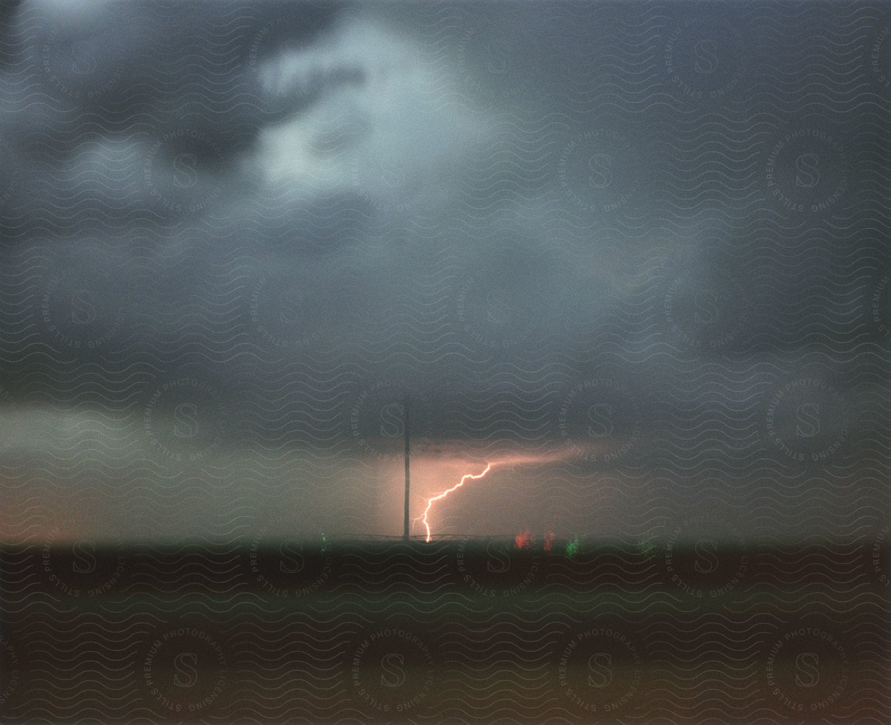 A lightning strike touching down in a wide open expanse with intense dark clouds