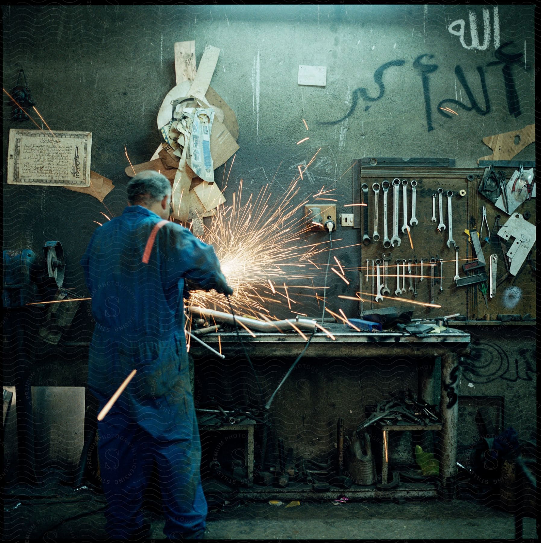 An old man in a uniform working in a workshop construction room with equipment and lighting