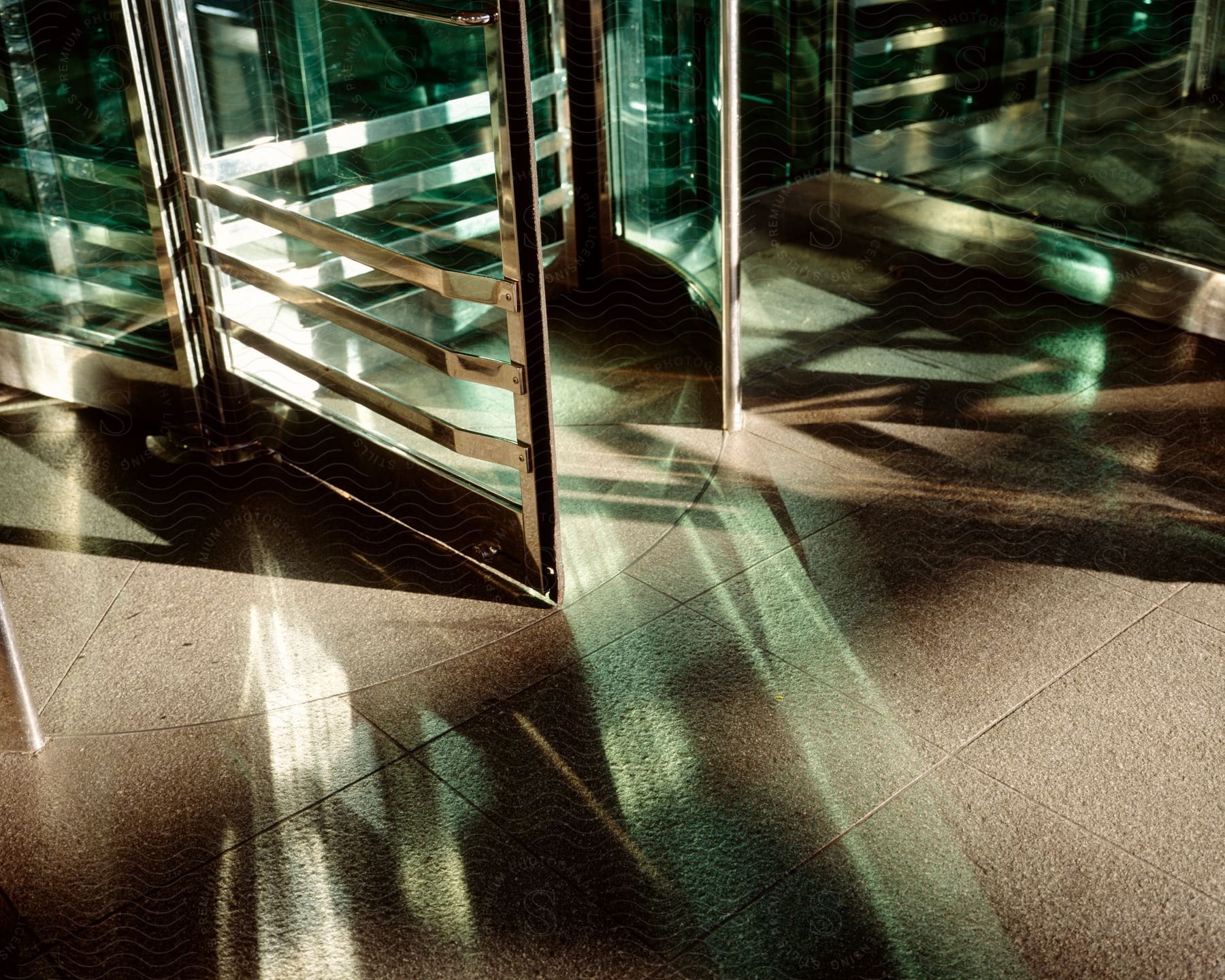 Light reflection is seen through a glass and metal turnstile door onto the concrete floor below in new york