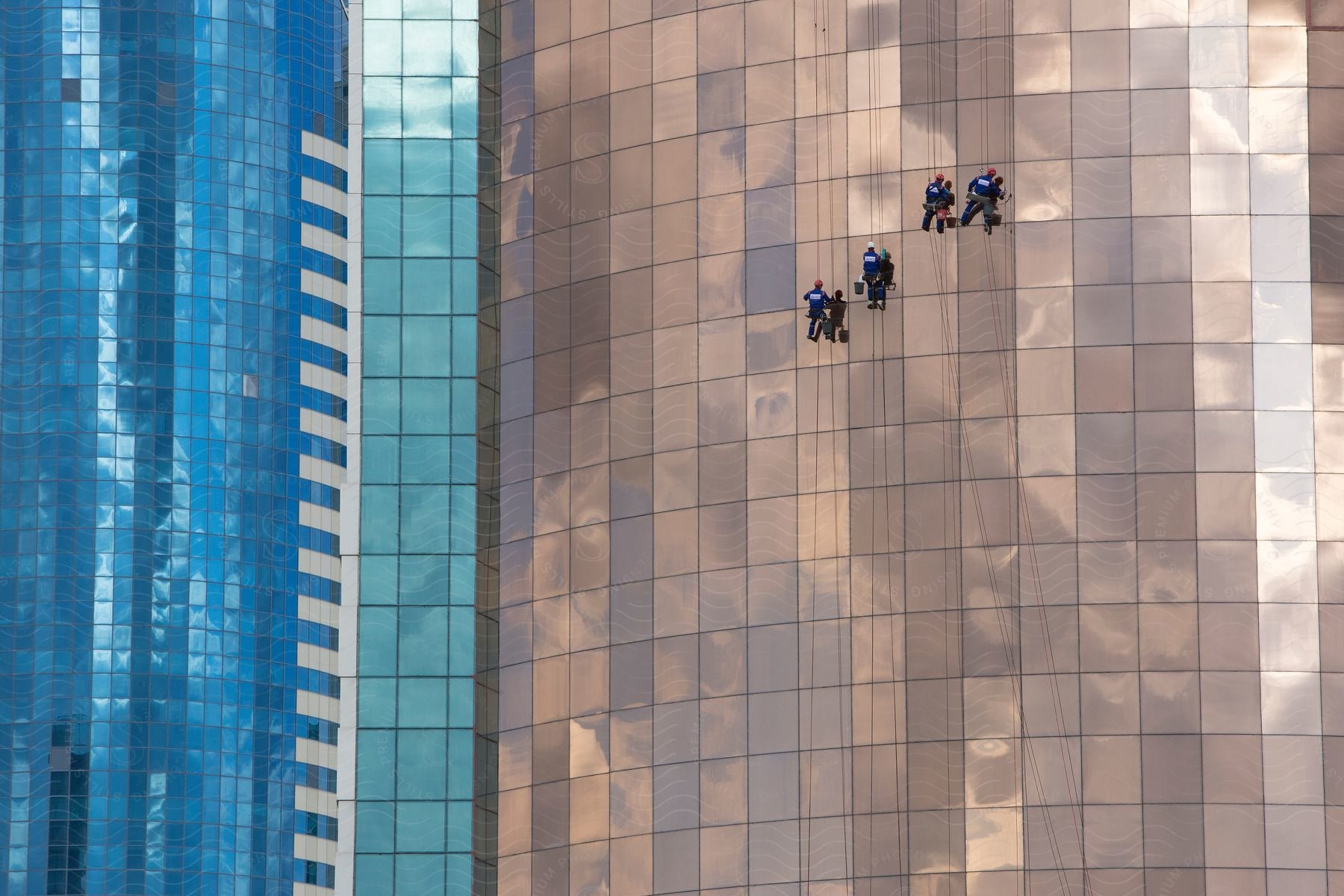 Four window cleaners hanging from ropes work on a skyscraper glass facade