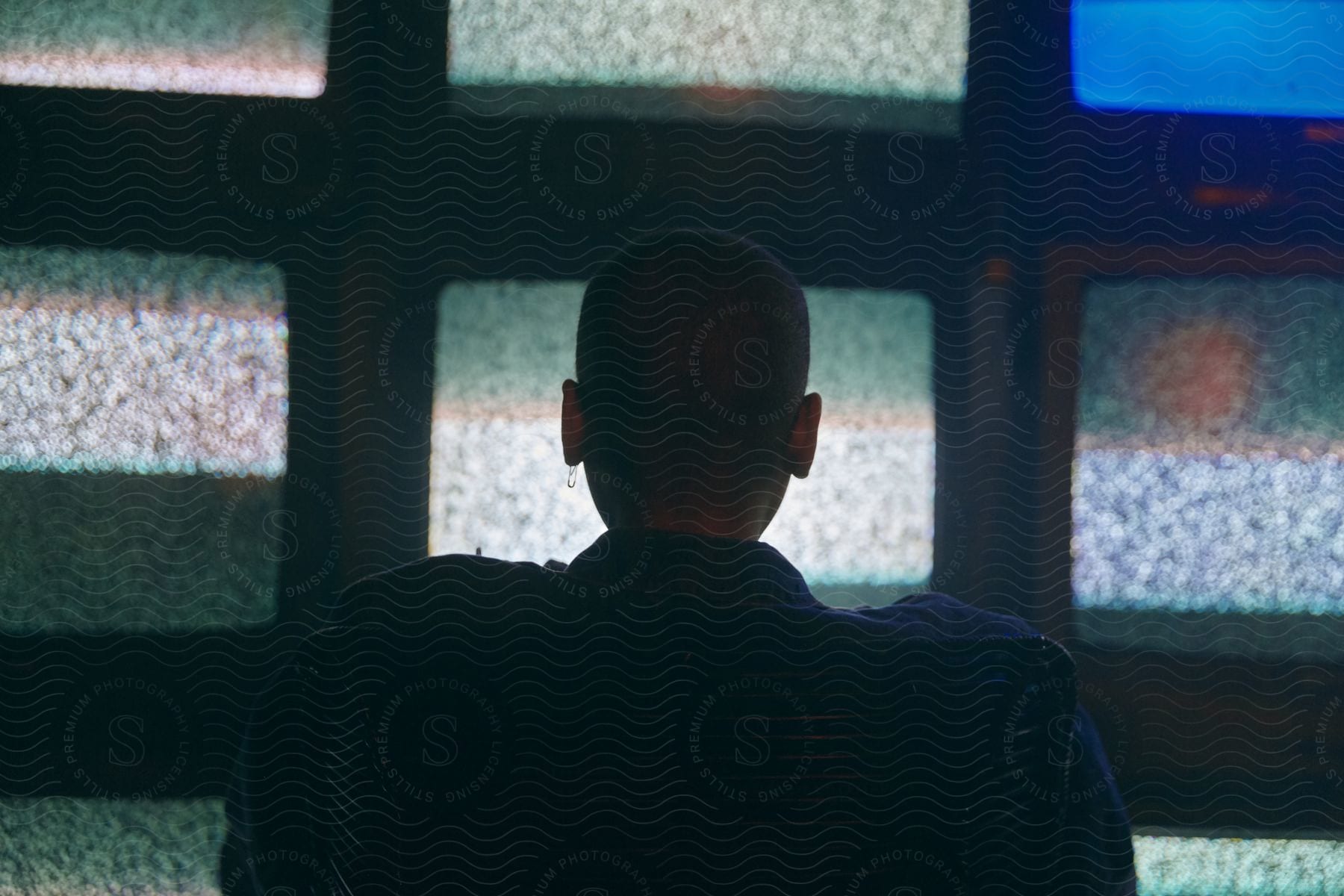 A man sits and stares at a bank of televisions showing static