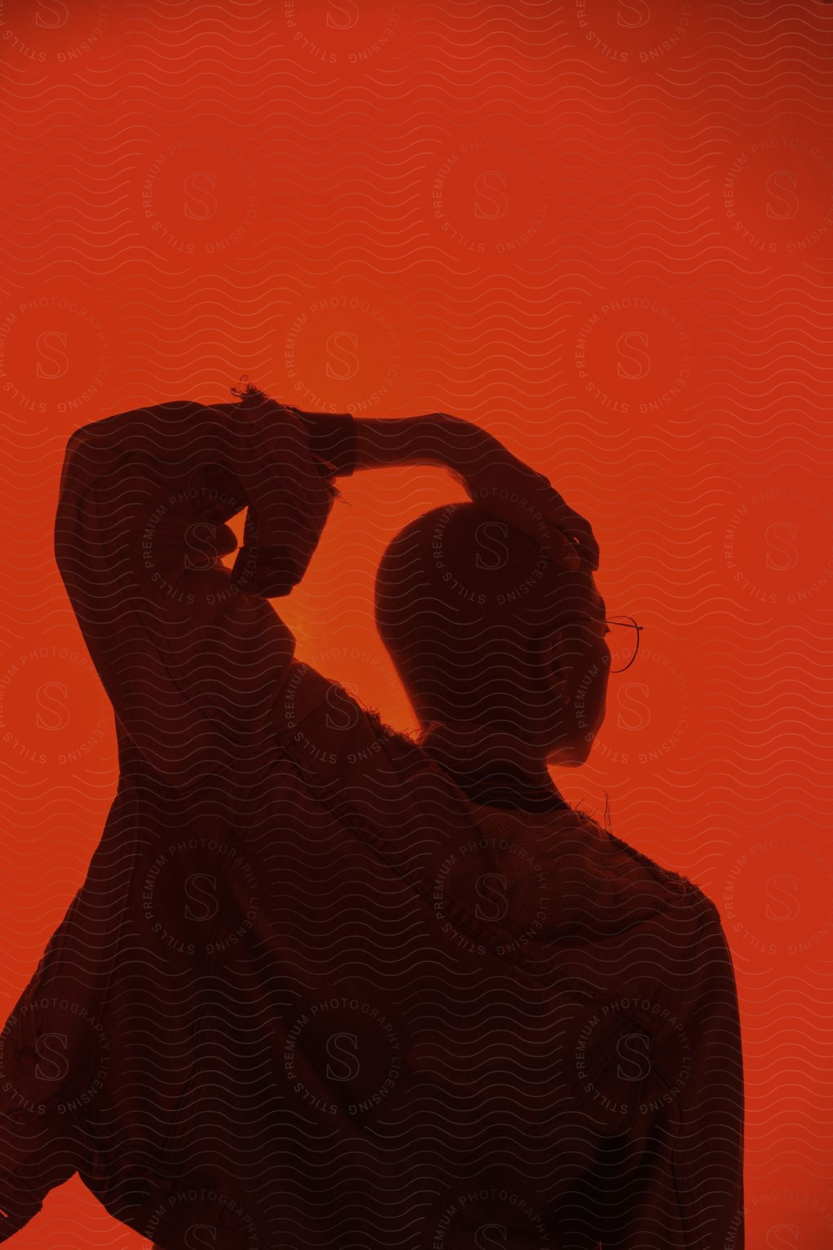 Boy in jean jacket and glasses with hand on head in front of red light background