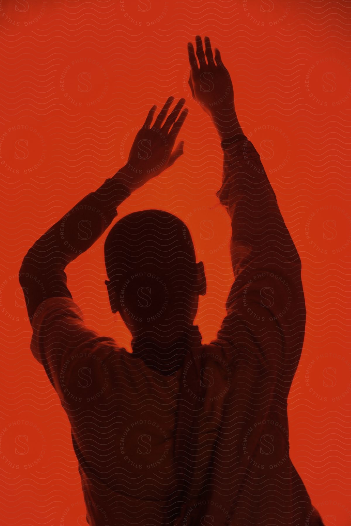 A person stands before a dim red background with their hands in the air having fun