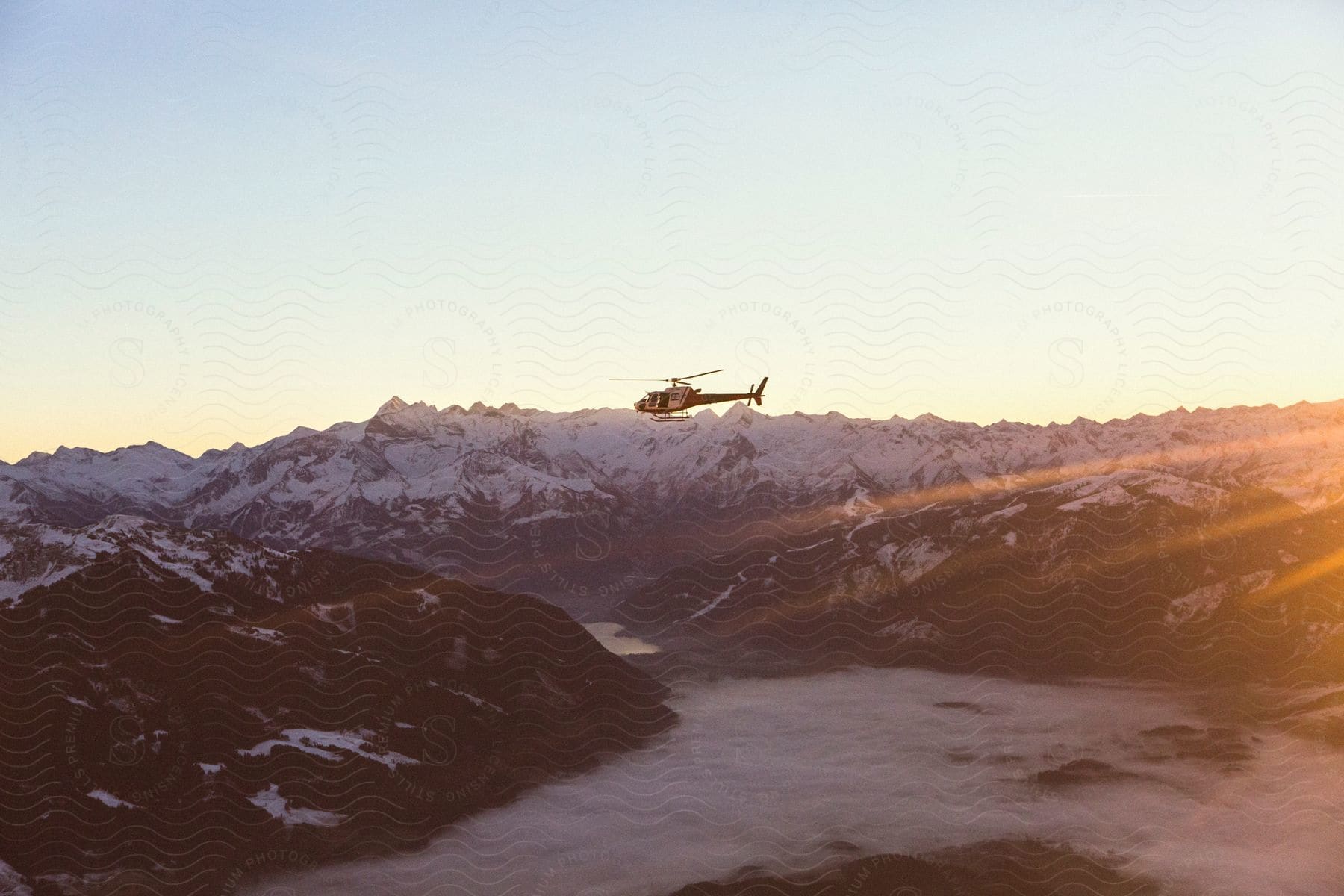 Helicopter flying over snowcovered mountains at sunset