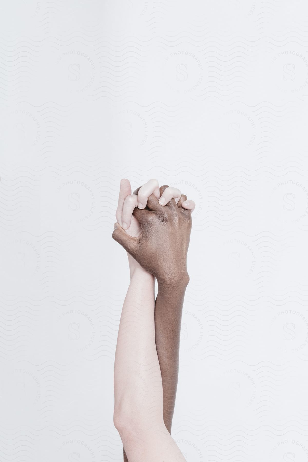 Two clasped hands of different skin tones on a white wall