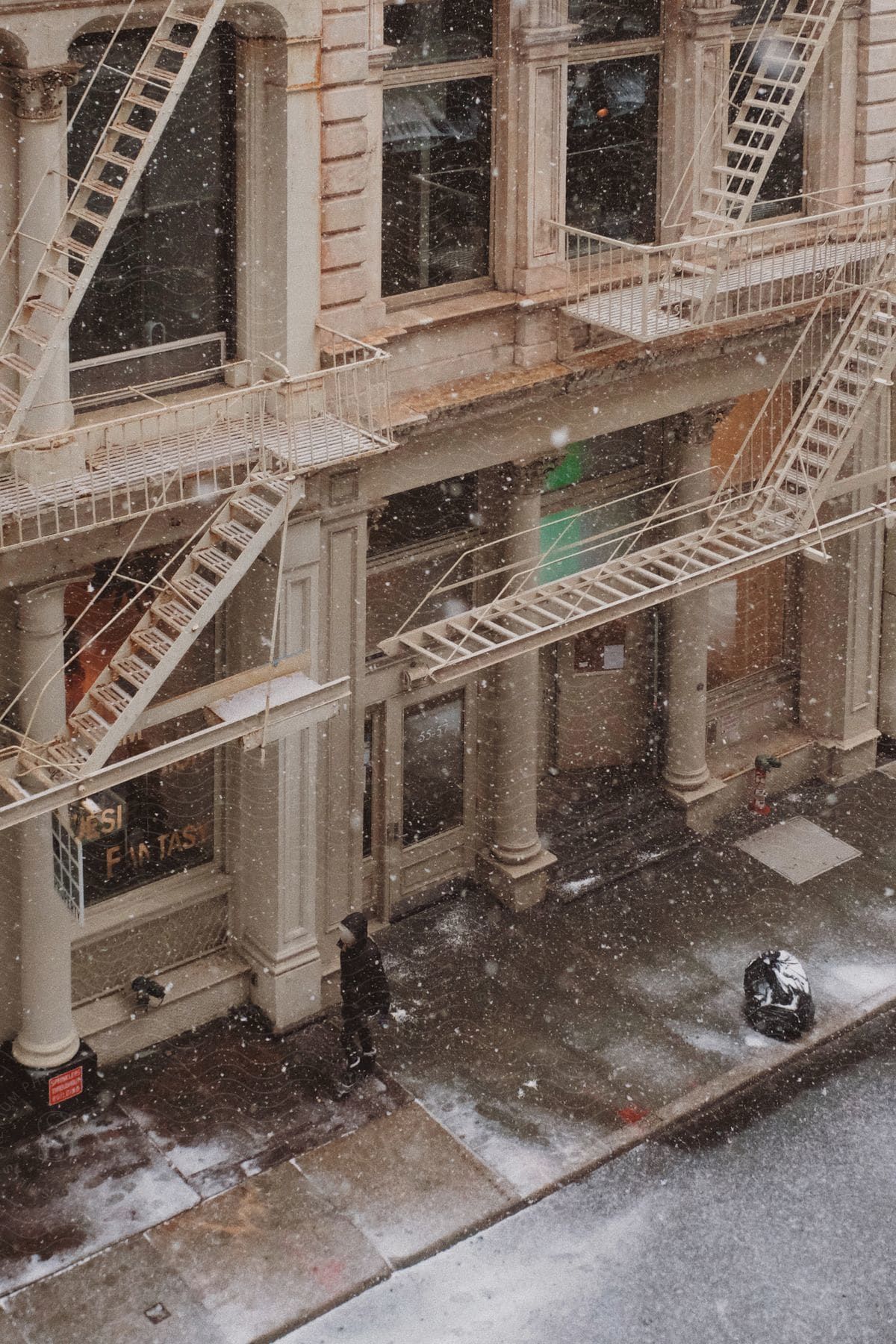 City street with snow falling old style building with large windows pillars and fire escape stairs